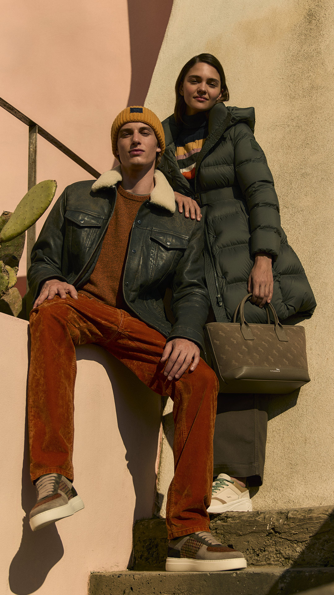 Paar in eleganten Herbst-Looks mit Lederjacke und schwarzer Daunenjacke.