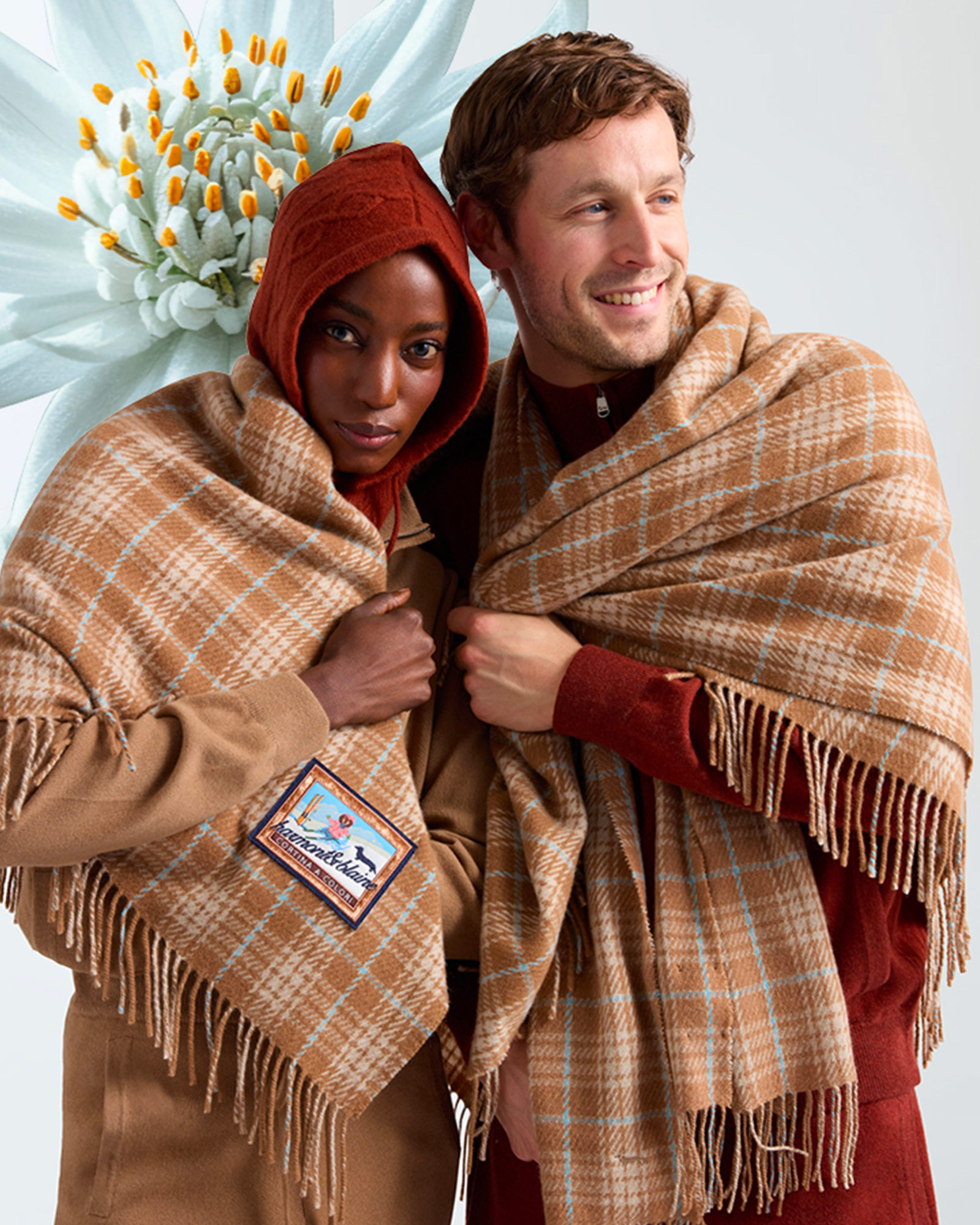 Woman and man wrapped in large beige and light blue checked scarves.