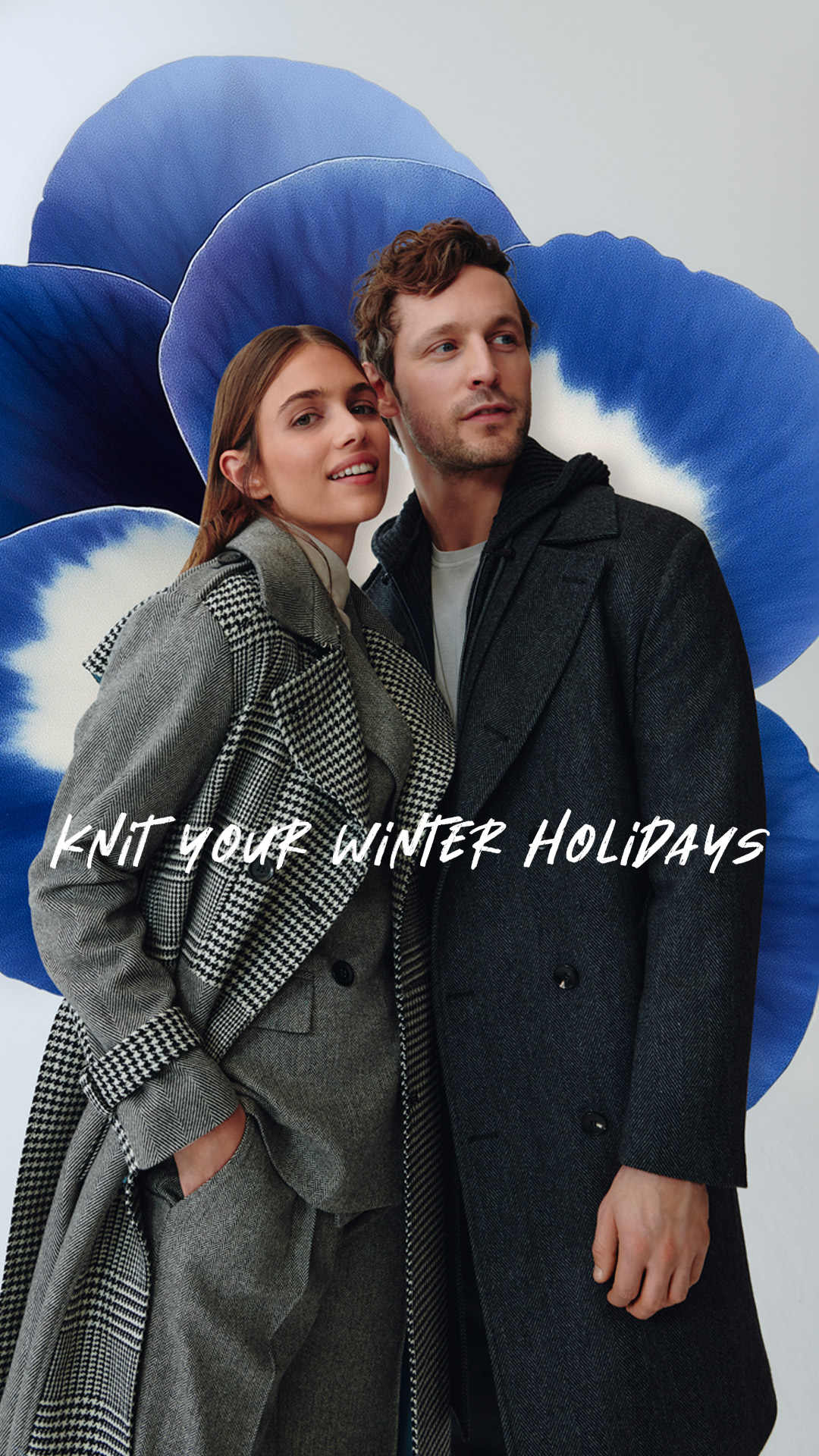 Pareja con abrigos de invierno frente a una gran flor azul.