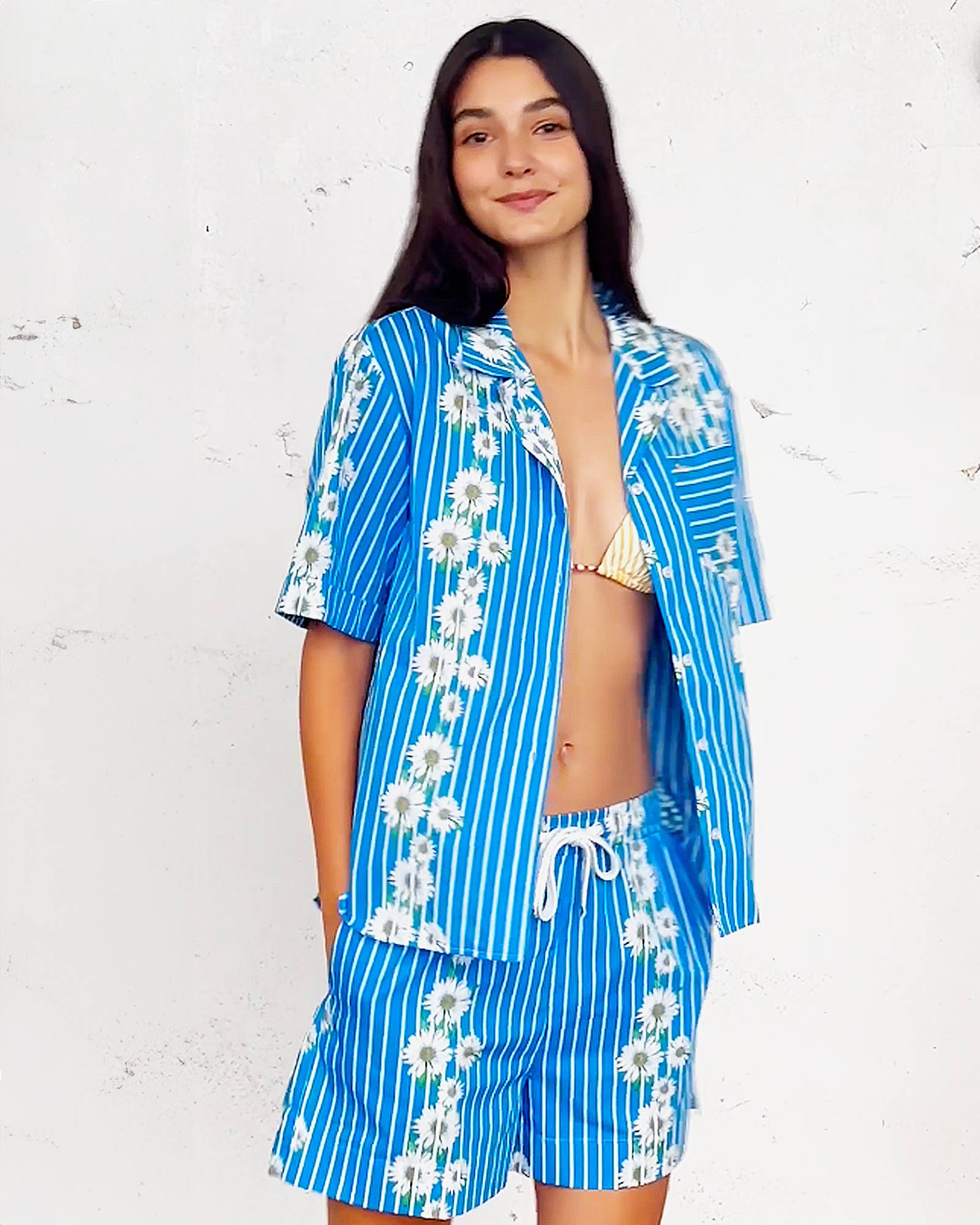 Mujer con conjunto veraniego a rayas azules y margaritas sobre fondo blanco.