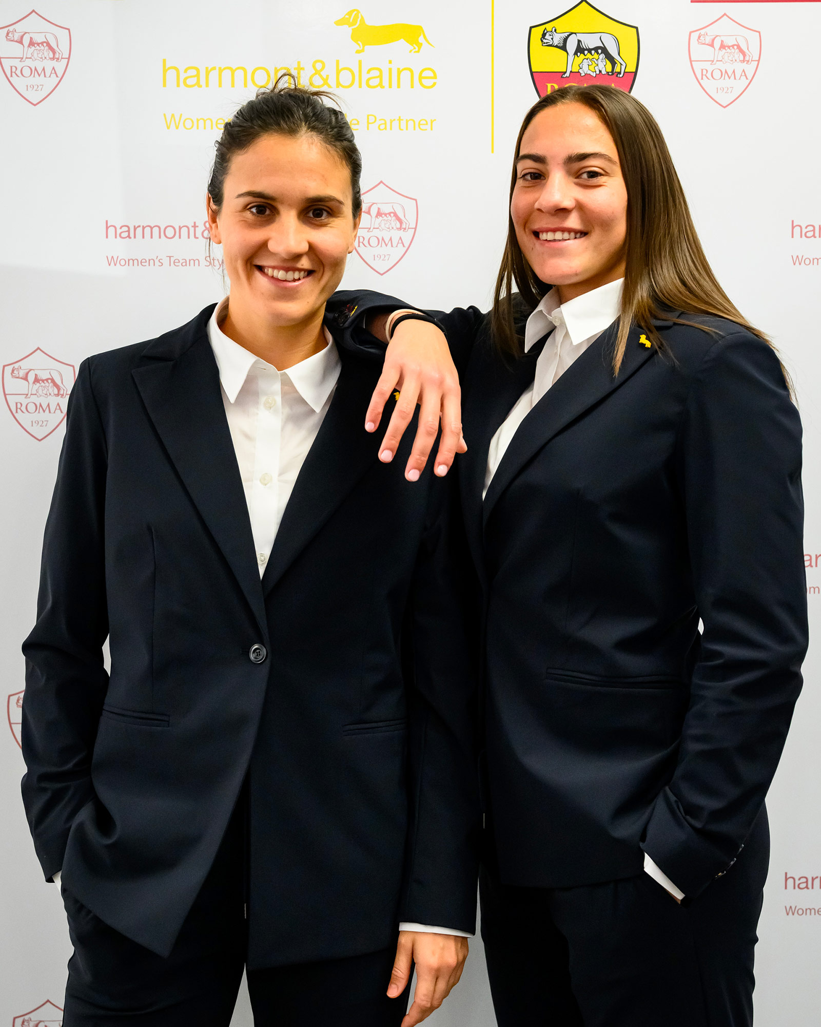 Due donne in completo blu navy con camicia bianca.