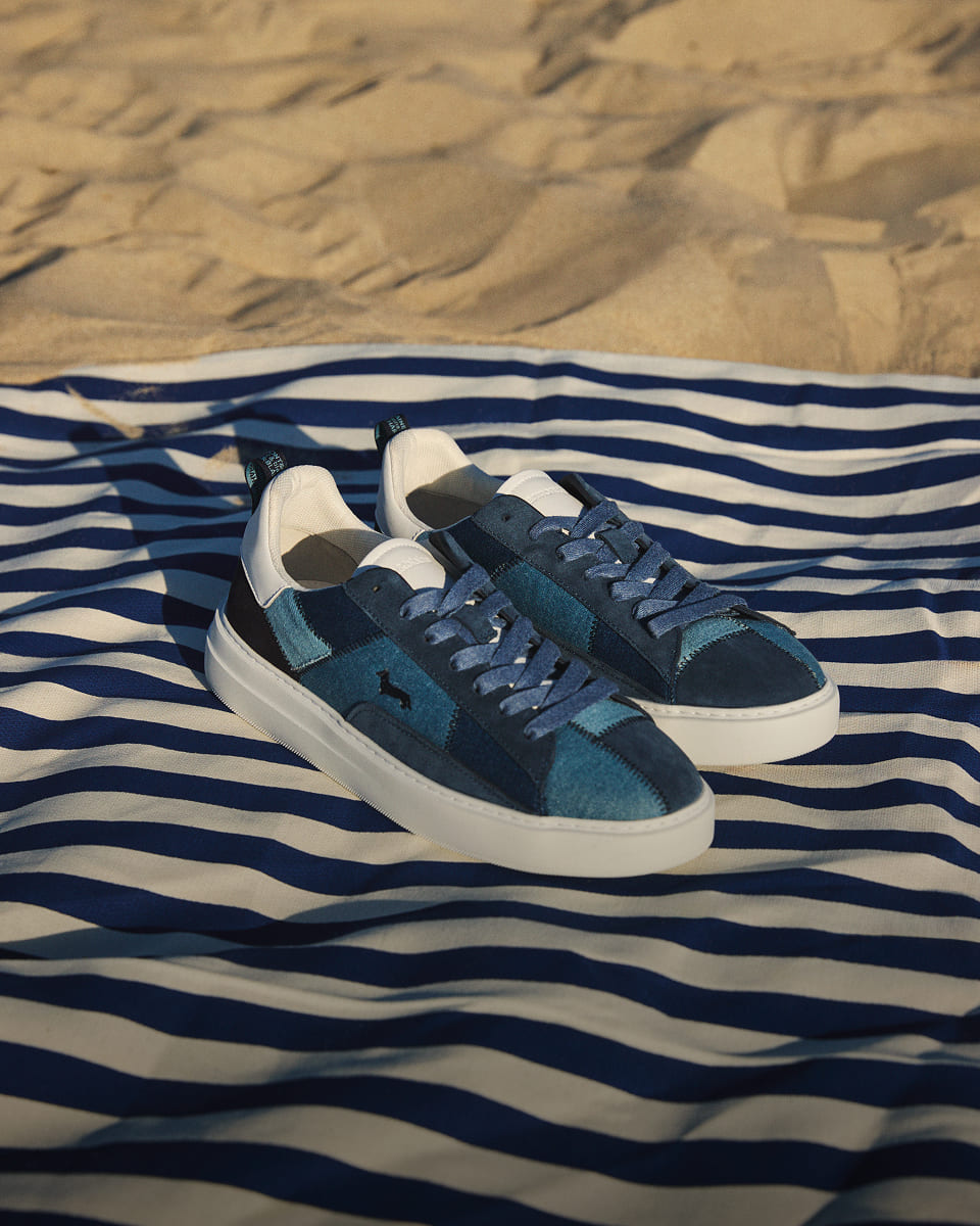 A pair of Harmont & Blaine patchwork sneakers resting on a blue and white striped beach towel with a sand background