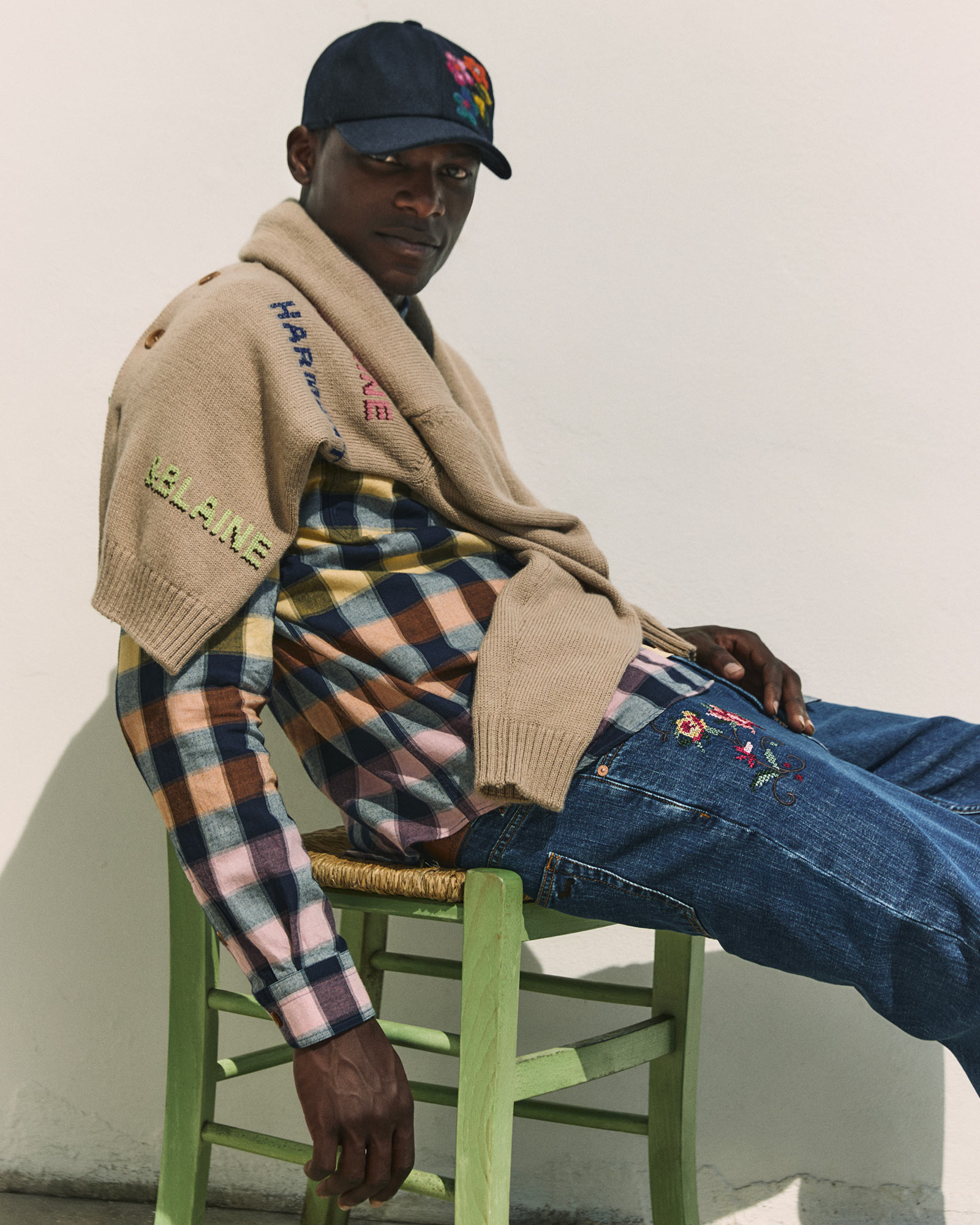 Model wearing a checked shirt with embroidered jeans and cap.