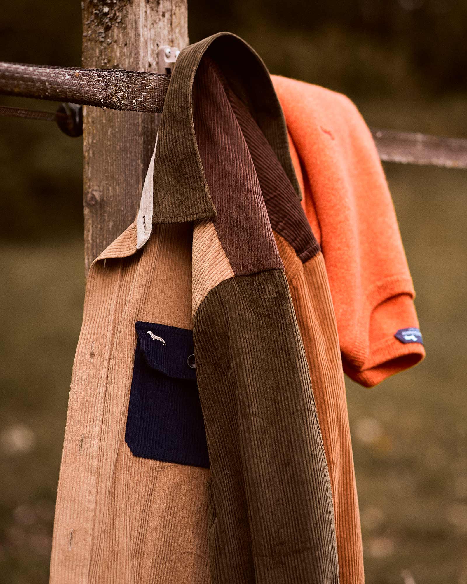 Dettaglio di overshirt in velluto a coste multicolore appesa a una staccionata.
