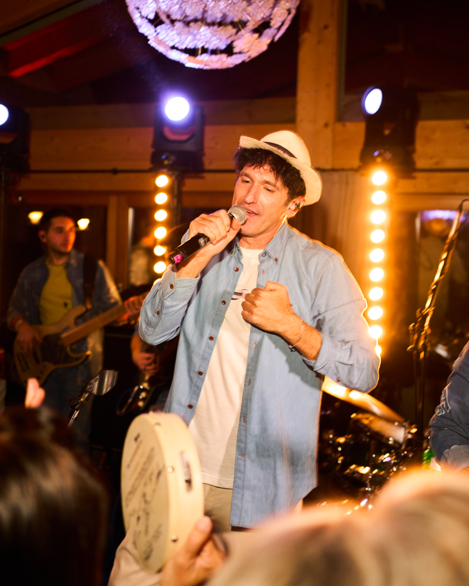 Cantante con camicia in denim e cappello chiaro mentre si esibisce sul palco.