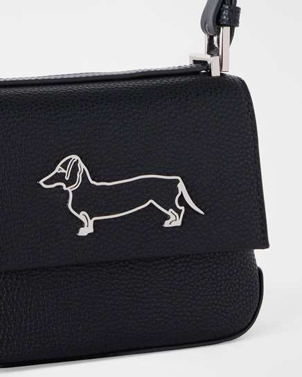 This promo image features a detailed close-up of a women's black pebbled leather crossbody bag, accented with a front flap featuring a silver-tone metal outline of the iconic Dachshund logo. The primary focus of the visual is to highlight Harmont & Blaine women's accessories, showcasing the premium leather craftsmanship, refined design, and sophisticated hardware of the collection.