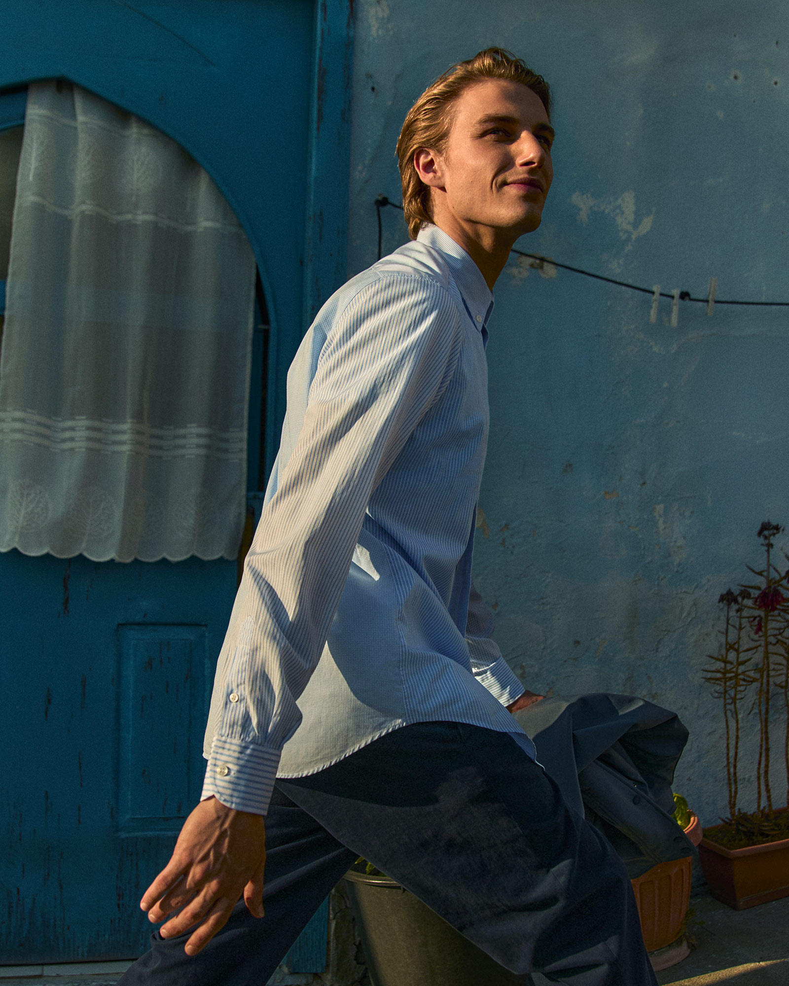 Man wearing a light blue striped shirt and dark trousers walking outdoors.