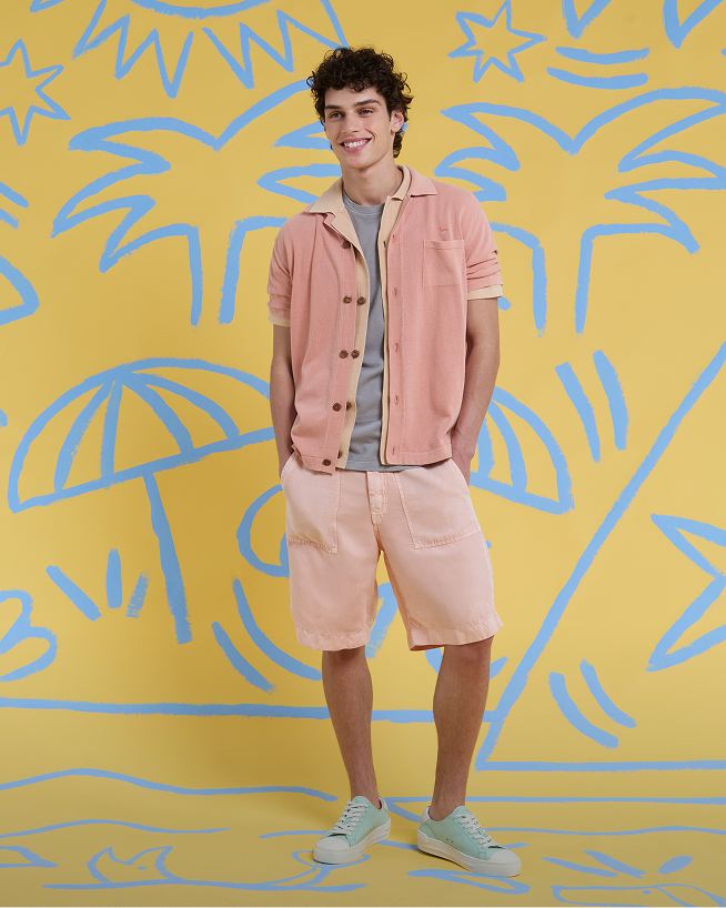 A man wearing a horizontally striped shirt in pastel tones and yellow bermuda shorts. Focus on bermuda shorts.