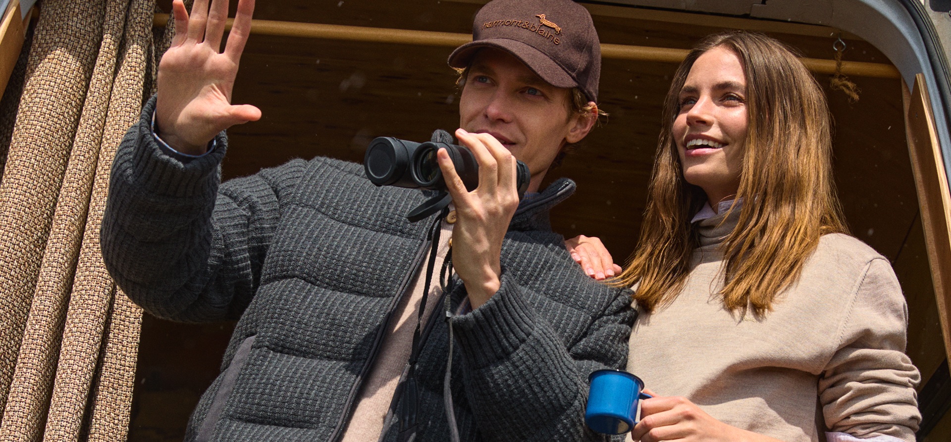 The promotional image for the Single's Day campaign shows a smiling young couple looking at the view from inside an outdoor-style van. The man is wearing a dark grey puffer jacket and a brown Harmont & Blaine cap while holding binoculars, while the woman beside him wears a beige sweater and holds a blue mug.