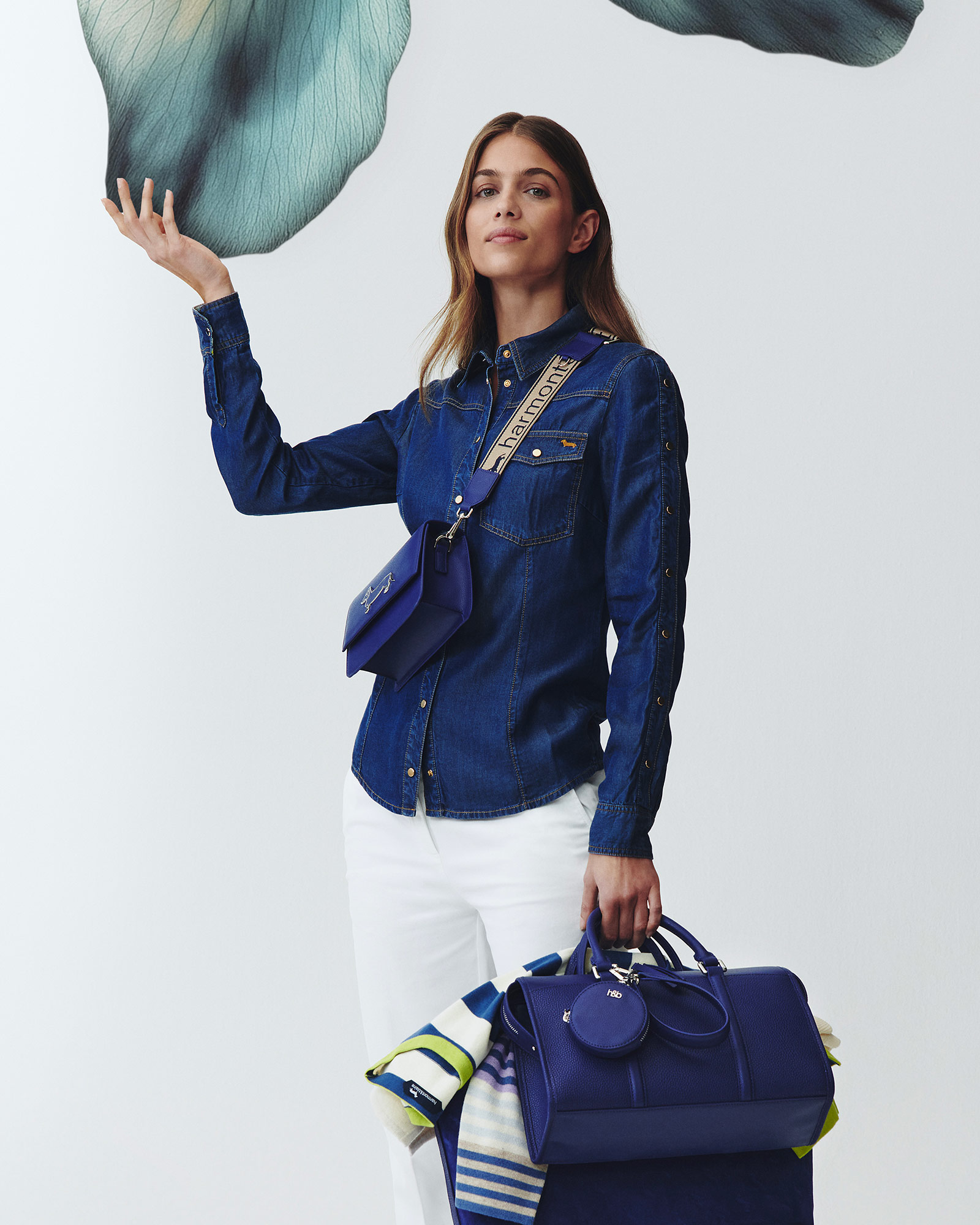 Donna con camicia di jeans, pantaloni bianchi e borse blu.