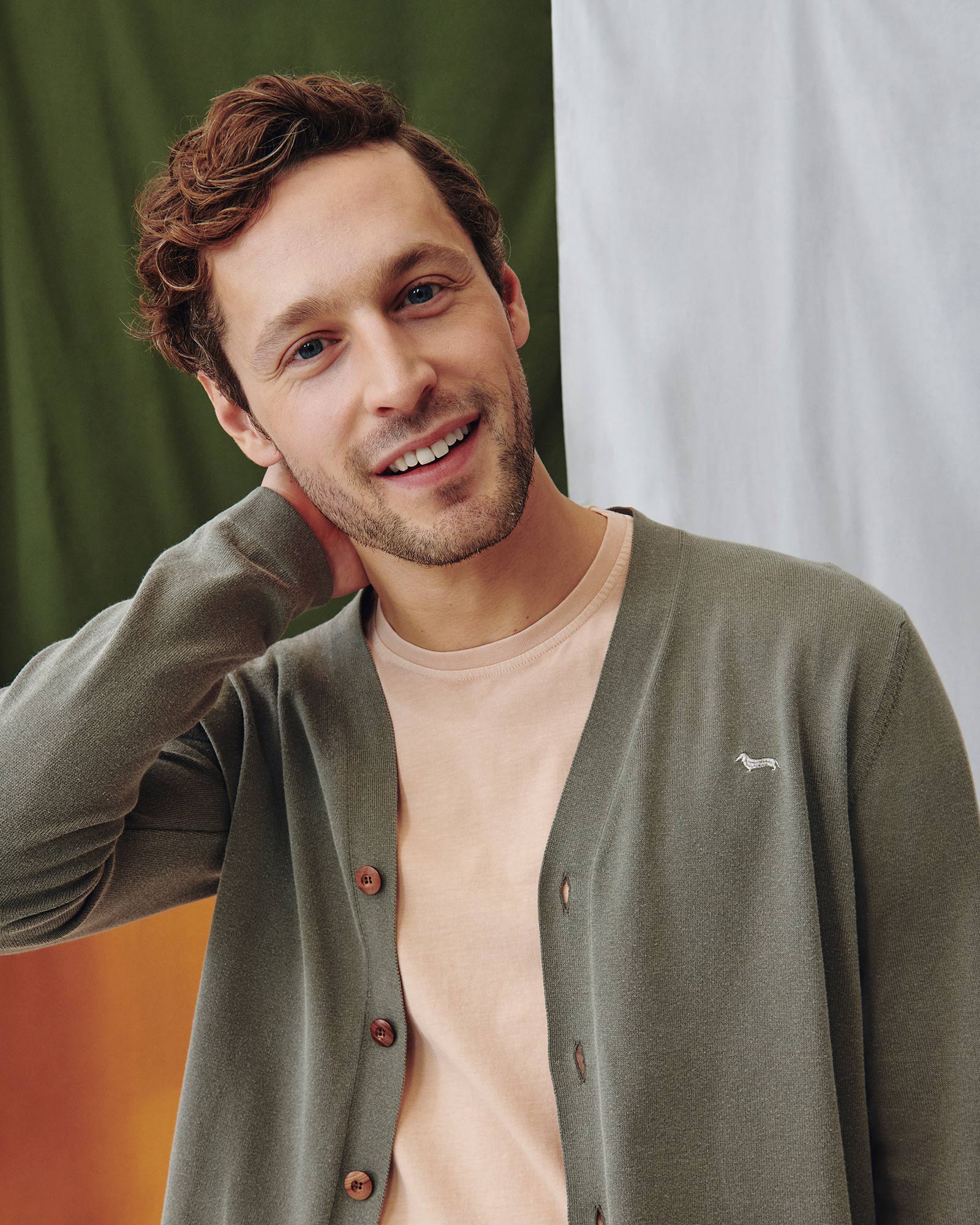 Close-up of male model wearing an olive green cardigan and peach t-shirt.