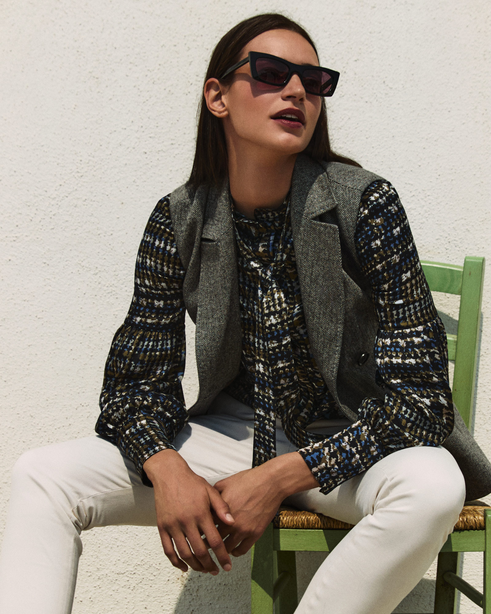 Donna con gilet in tweed grigio e camicia fantasia con pantaloni bianchi