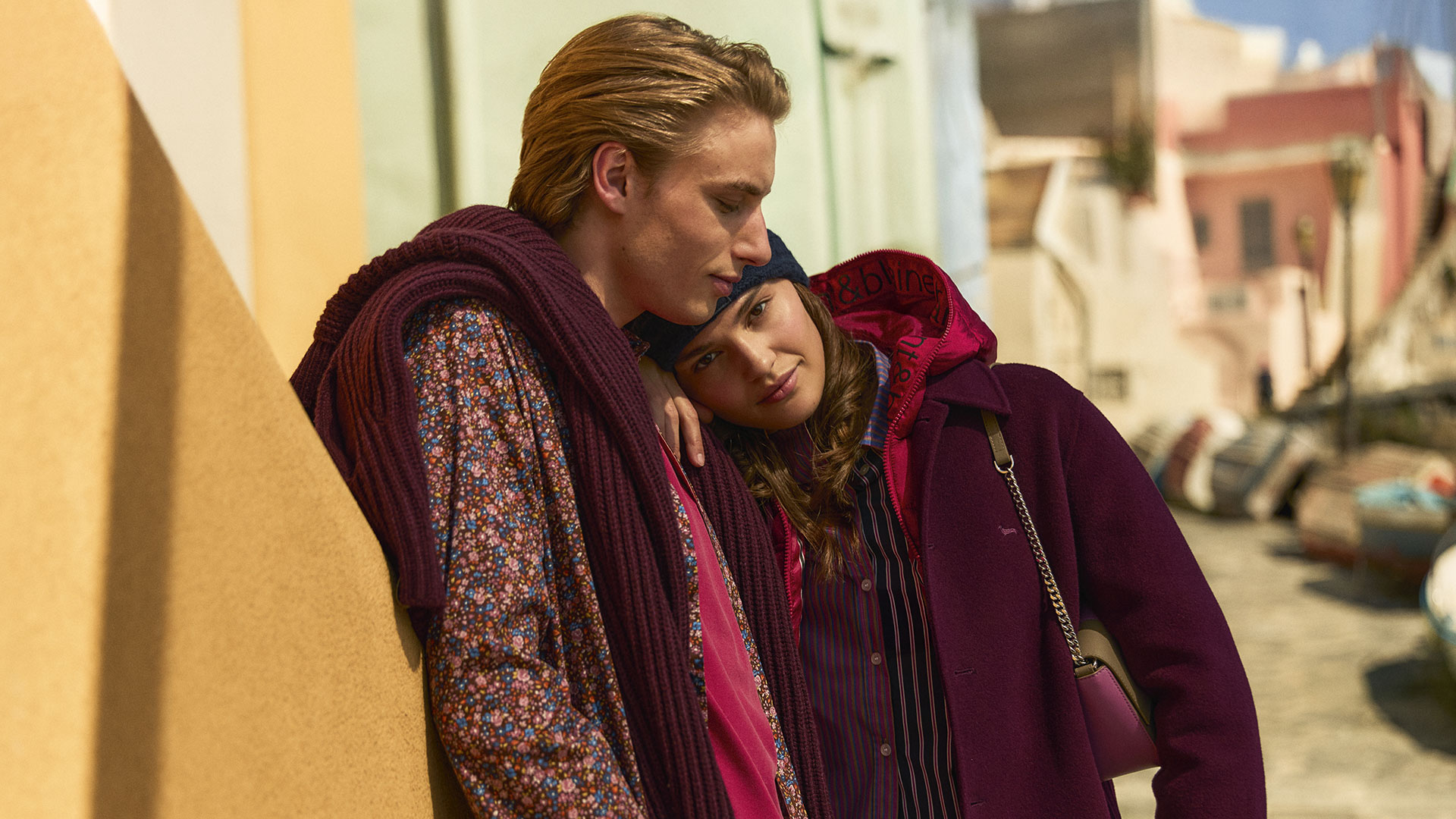 Coppia in look autunnali eleganti con cappotto bordeaux e camicia floreale.