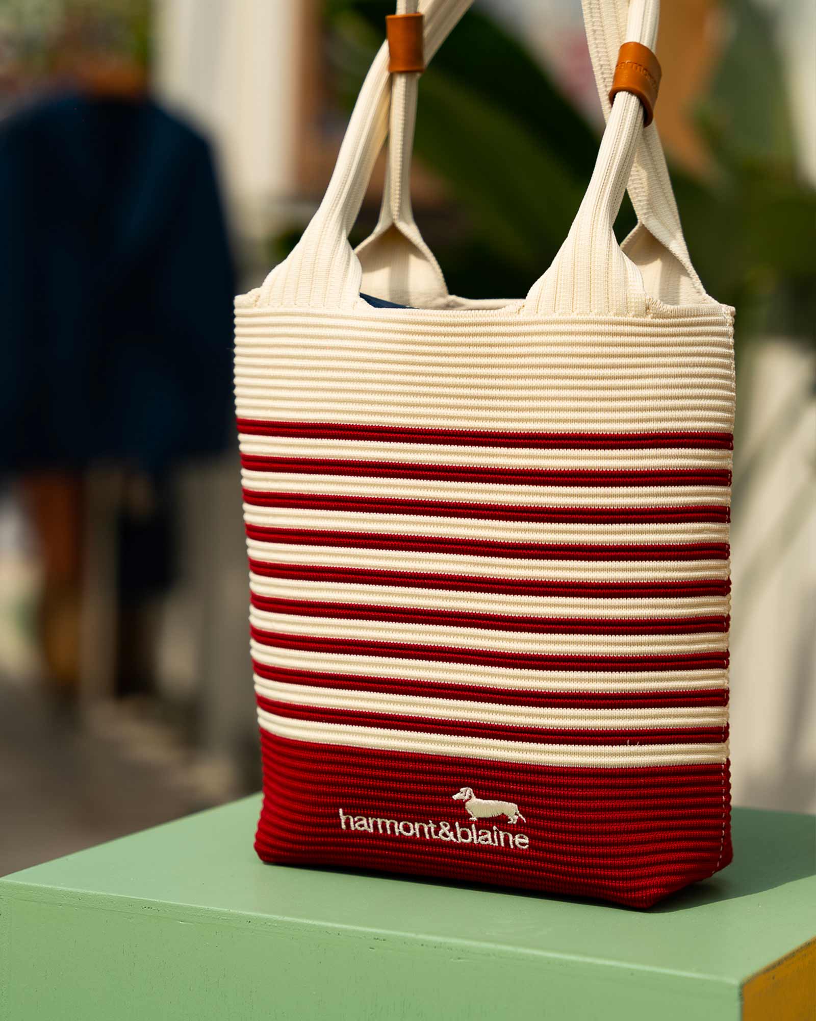 Striped red and cream tote bag with wooden handles and Harmont & Blaine logo, displayed on a pastel green surface — elegant and functional summer accessory.