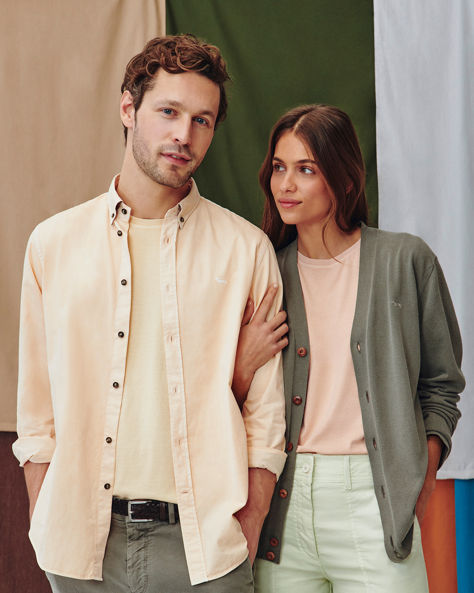 Modello uomo con camicia color pesca e modello donna con cardigan verde oliva e t-shirt rosa.
