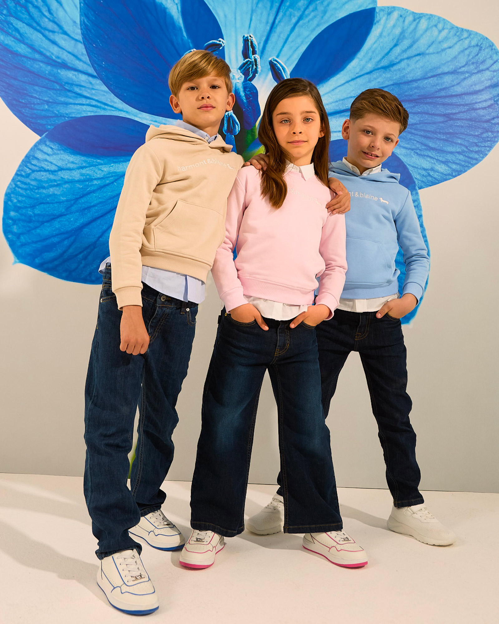 Kids wearing beige, pink, and light blue hoodies paired with dark jeans.