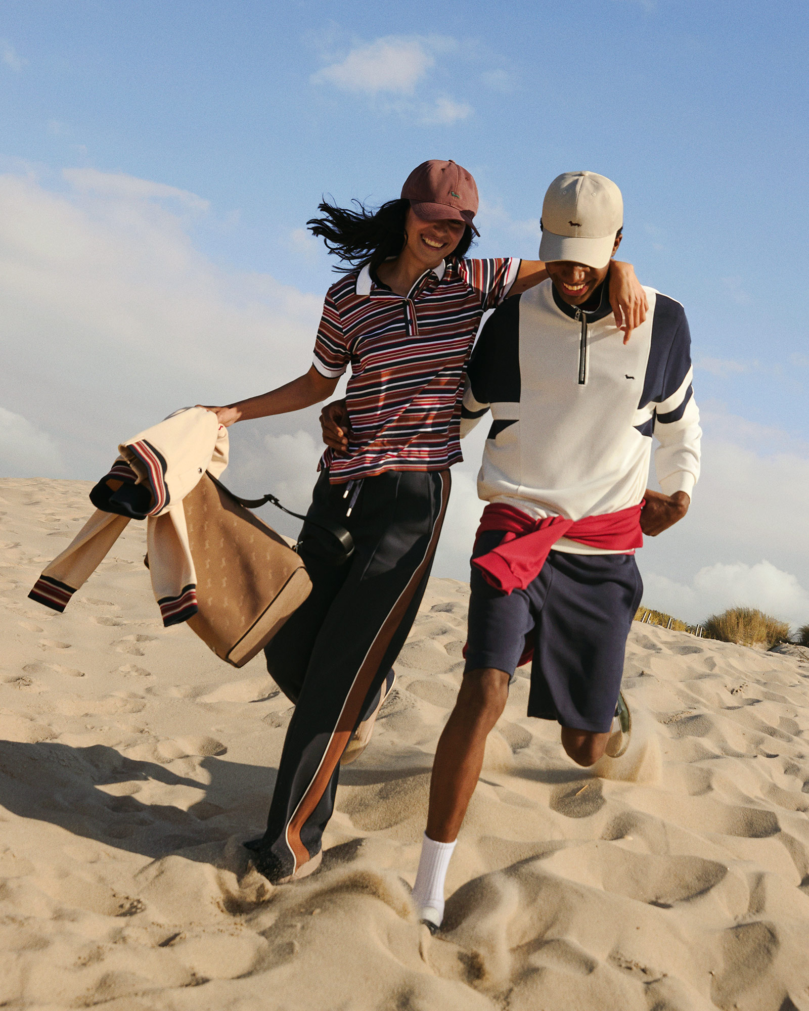 Coppia in spiaggia con polo a righe e cappellini da baseball