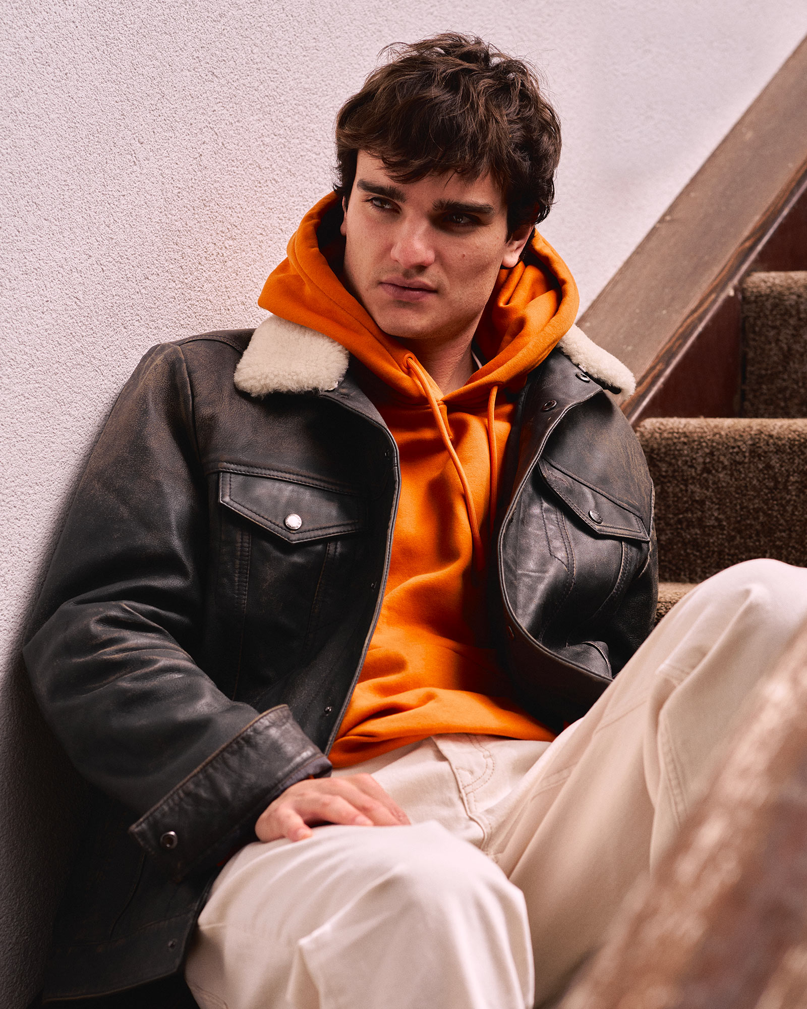 Person indoors wearing a dark coat, neutral background