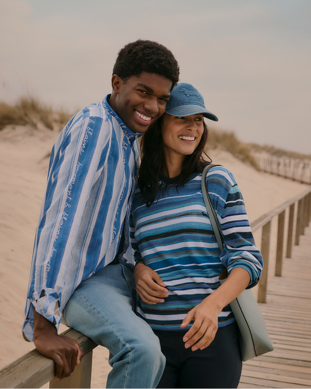 Coppia in spiaggia con polo a righe e cappellini da baseball