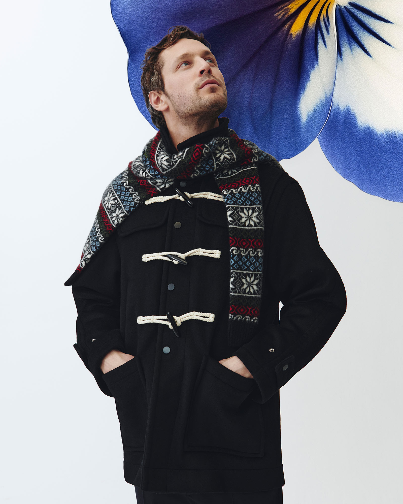 Man wearing a black duffle coat and a multicolour jacquard scarf.