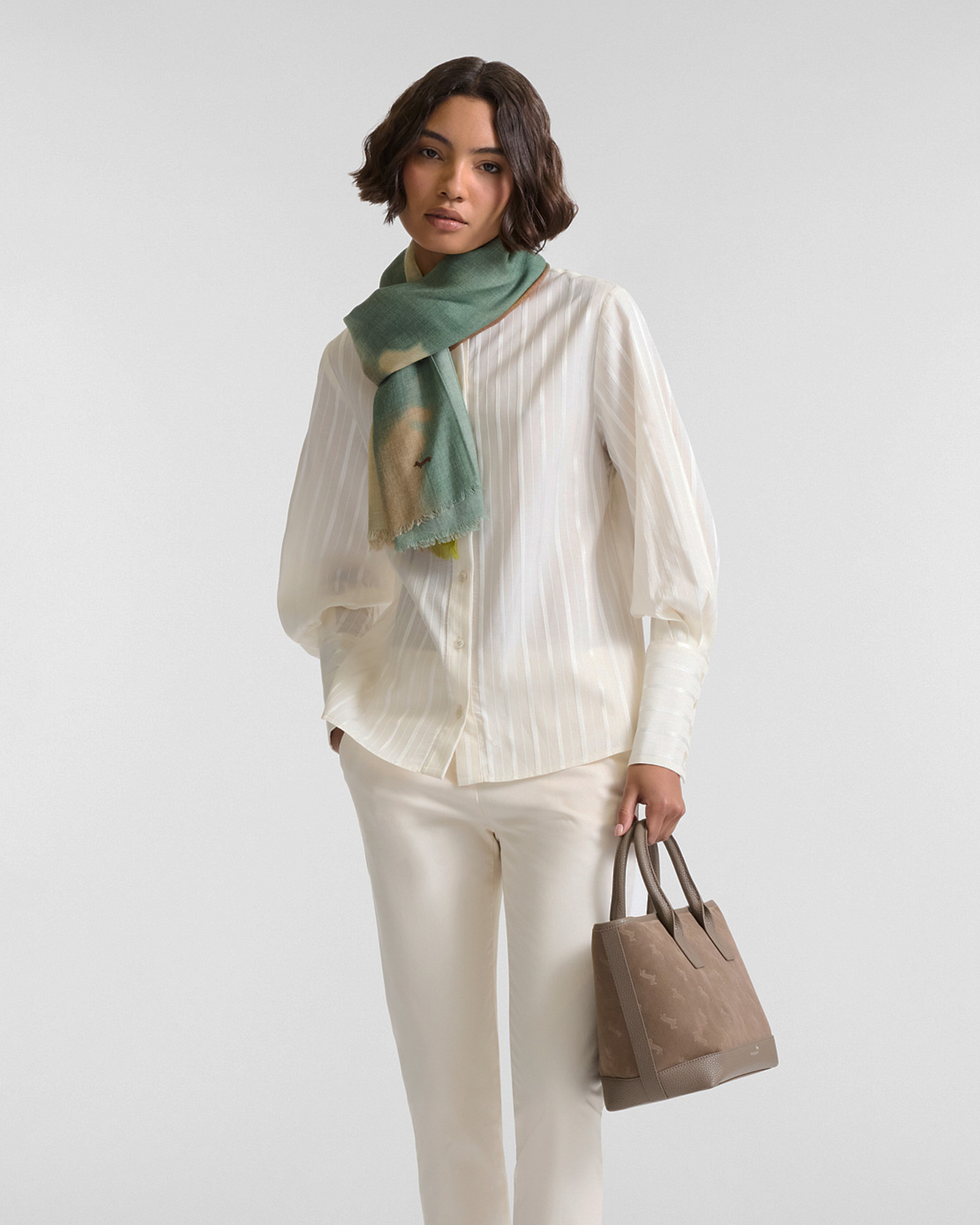 Donna con camicia bianca a righe leggere, pantaloni chiari, sciarpa verde e borsa beige