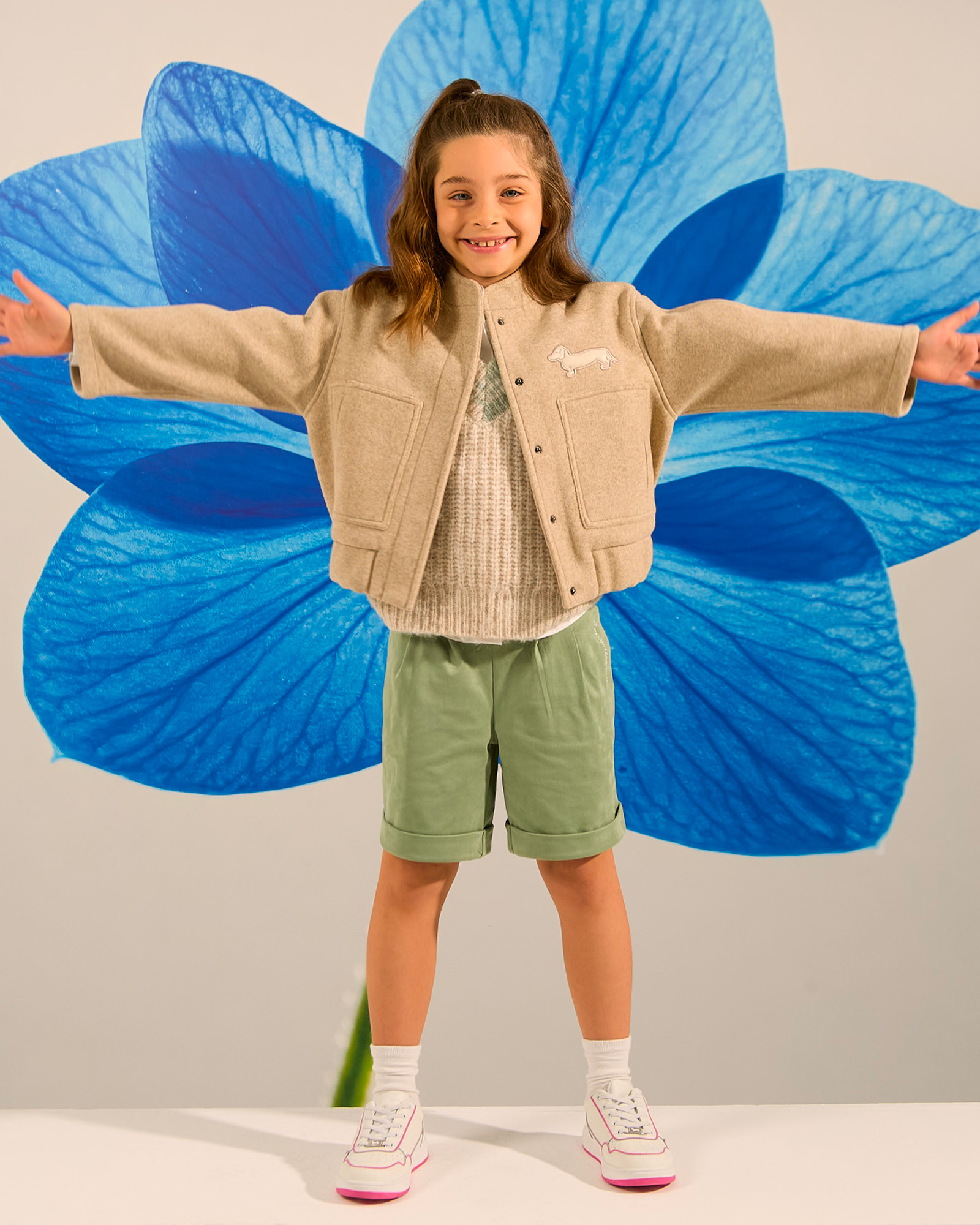 Girl in beige jacket, light sweater, green bermuda shorts and white sneakers