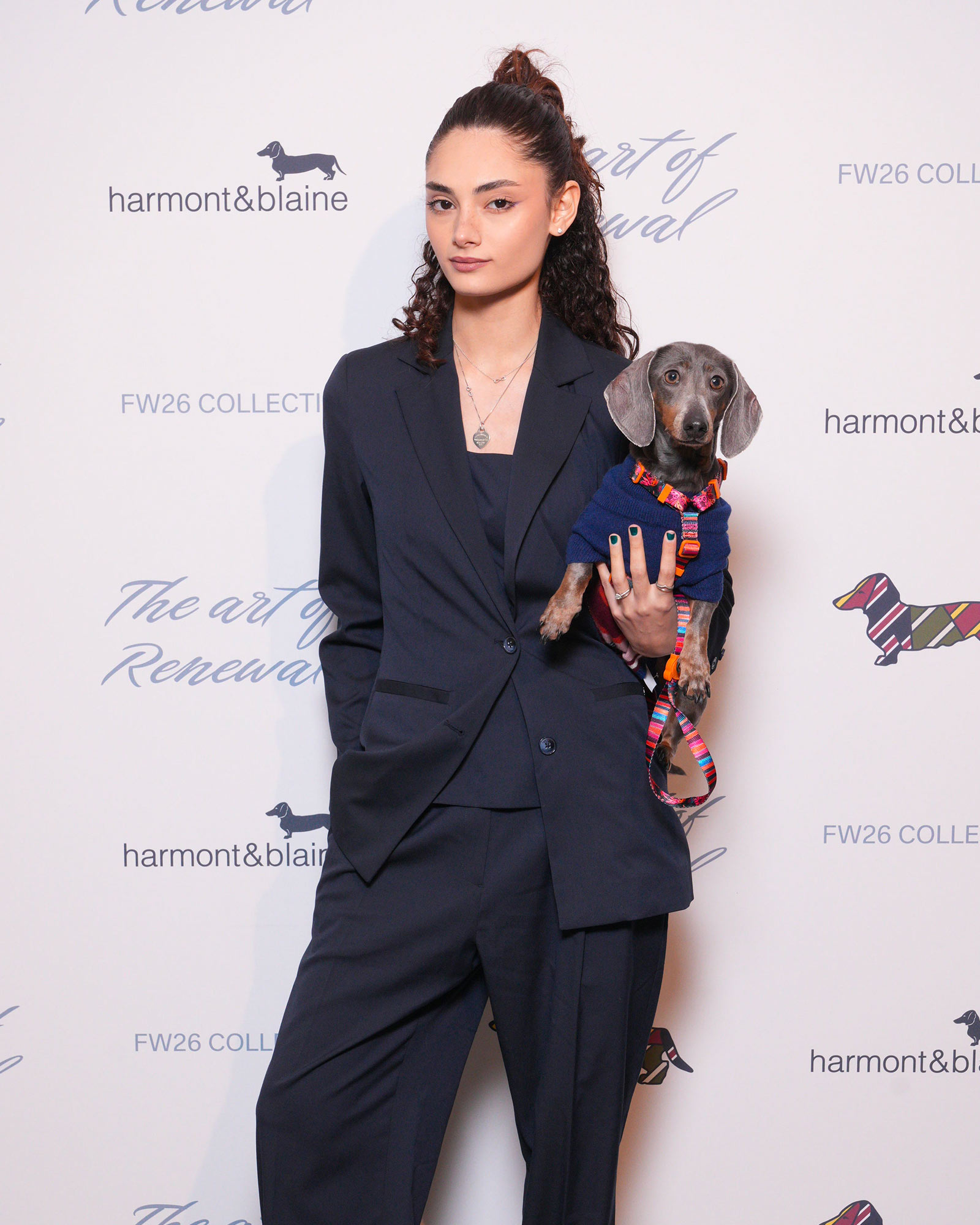 Donna con completo scuro e bassotto in maglioncino colorato