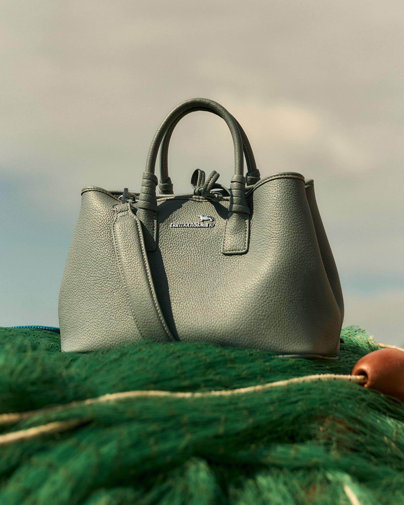 Gray leather handbag placed on a green fishing net.