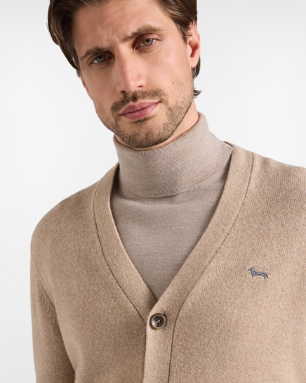 Un modello indossa un cardigan beige con scollo a V e abbottonatura frontale sopra un dolcevita coordinato Harmont & Blaine, arricchito dal caratteristico logo del bassotto ricamato sul petto, in un'immagine focalizzata sulla categoria maglieria uomo.