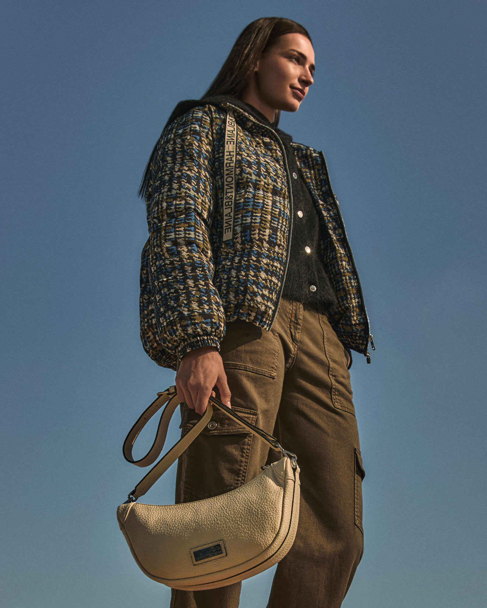 Woman wearing a patterned jacket, brown cargo pants, and a cream shoulder bag.