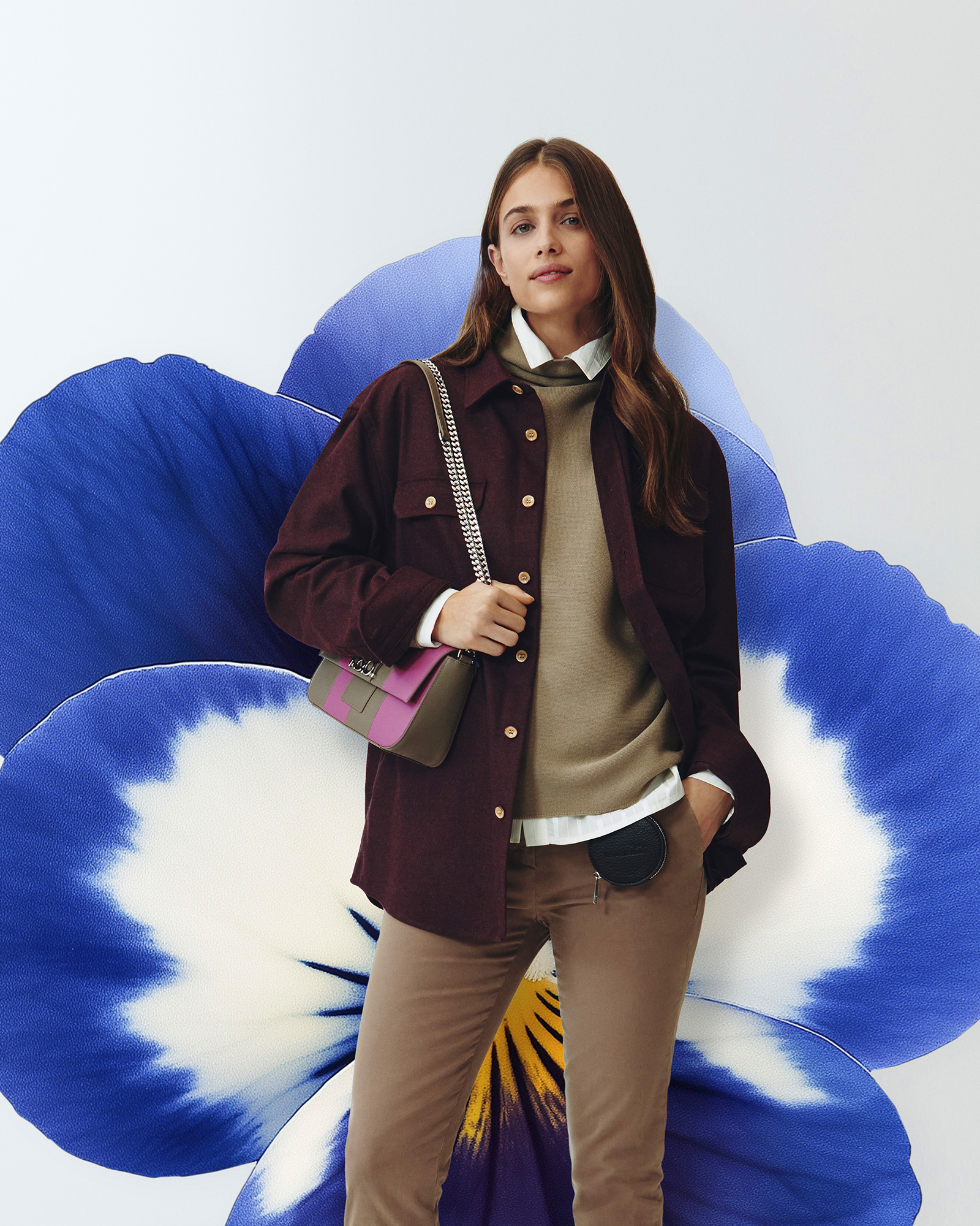 Donna con camicia bordeaux, maglione beige e pantaloni marroni, borsa a tracolla con catena