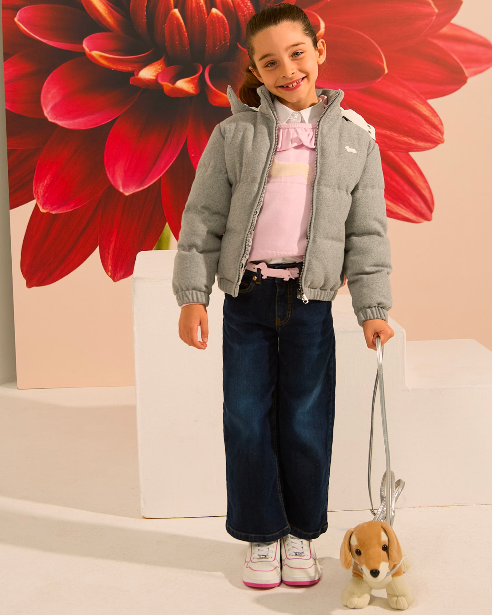 Bambina con giacca imbottita e peluche, fiore rosso dietro.