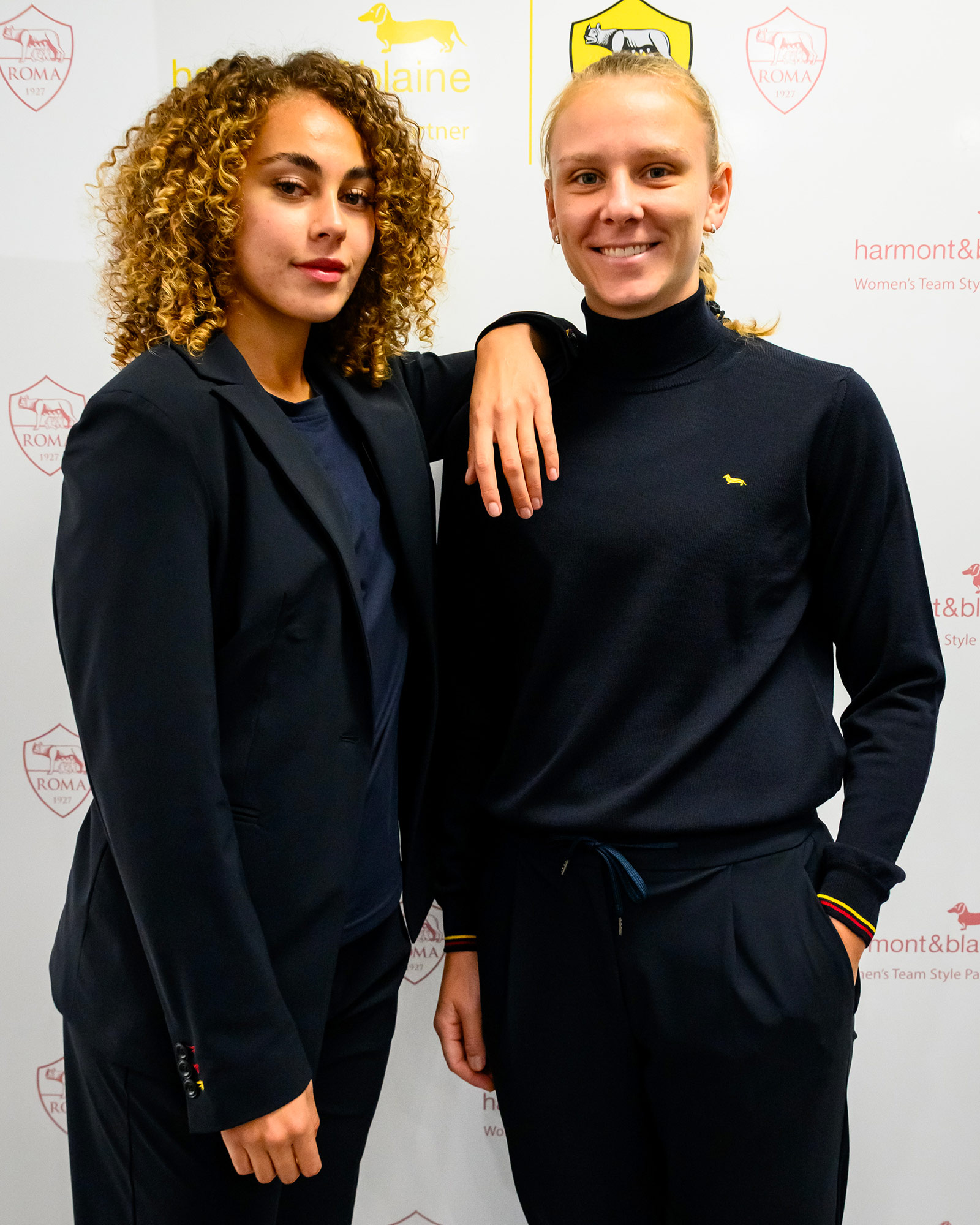 Due donne in uniforme blu navy, una con dolcevita e l’altra con blazer.