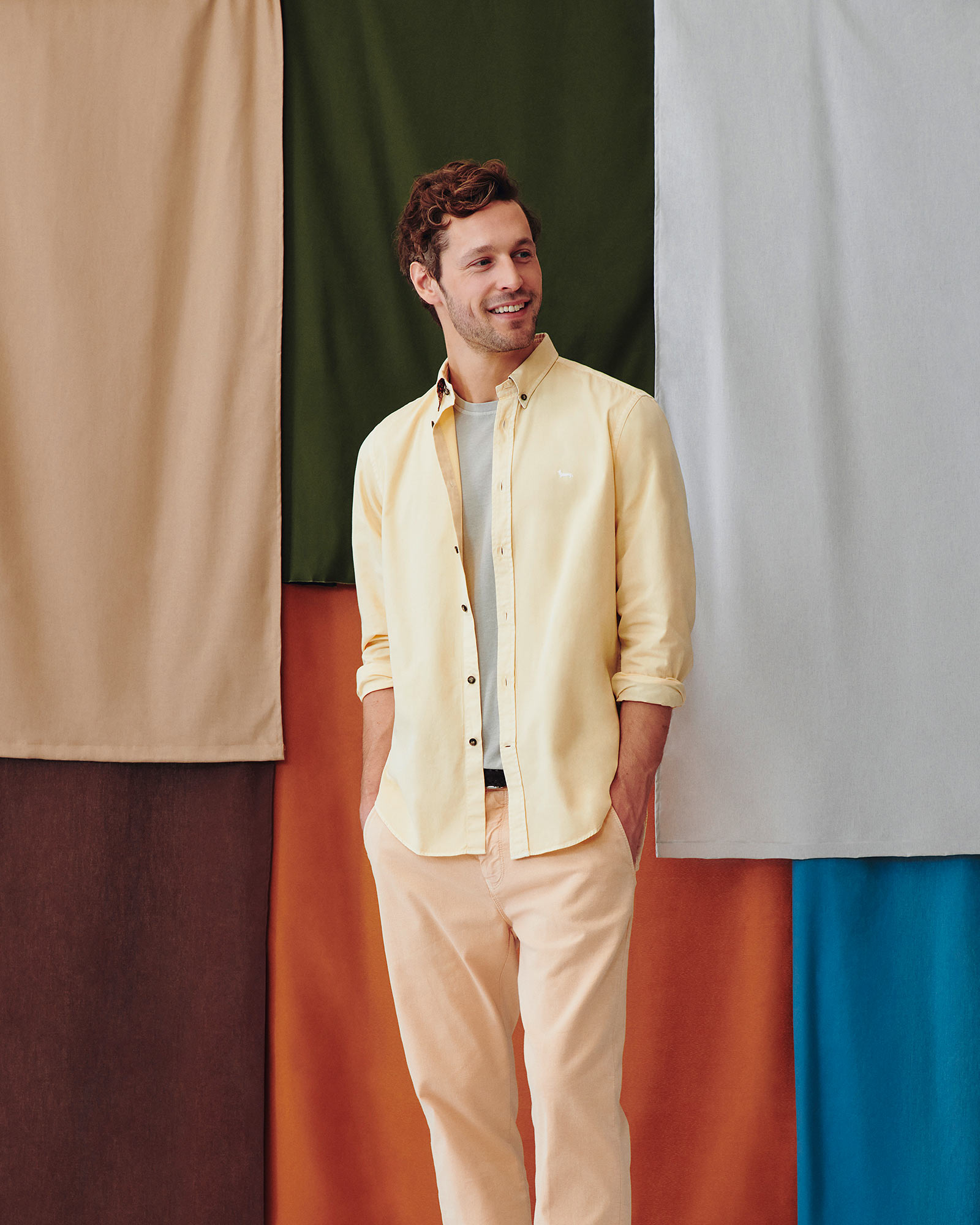 Modello uomo con camicia gialla e pantaloni color pesca su sfondo colorato.