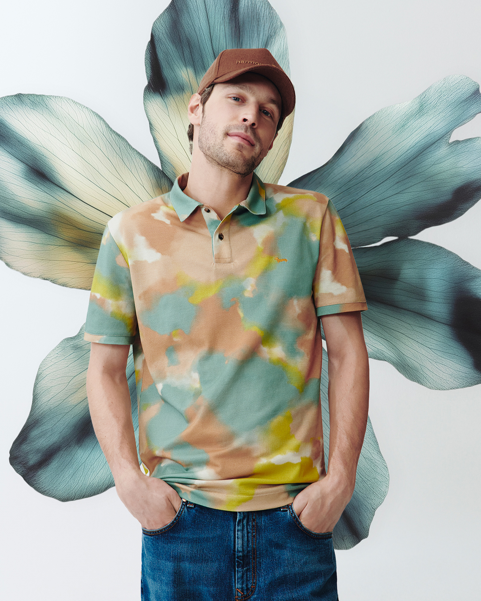 Man wearing a beige and green gradient print polo shirt and a brown cap.