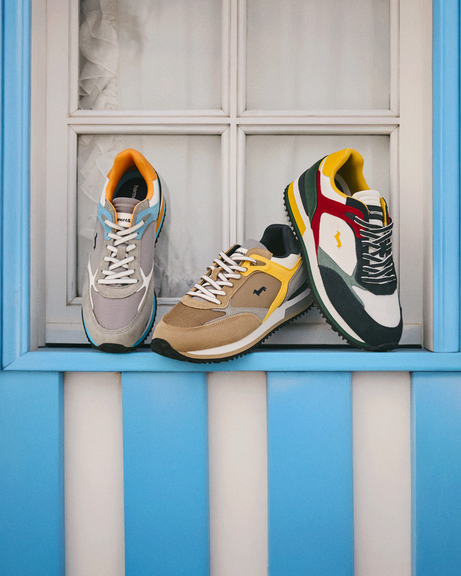 Tre giovani amici seduti su un divano, sorridenti e rilassati con outfit casual a strati &mdash; atmosfera autentica e conviviale in stile HB Magazine.