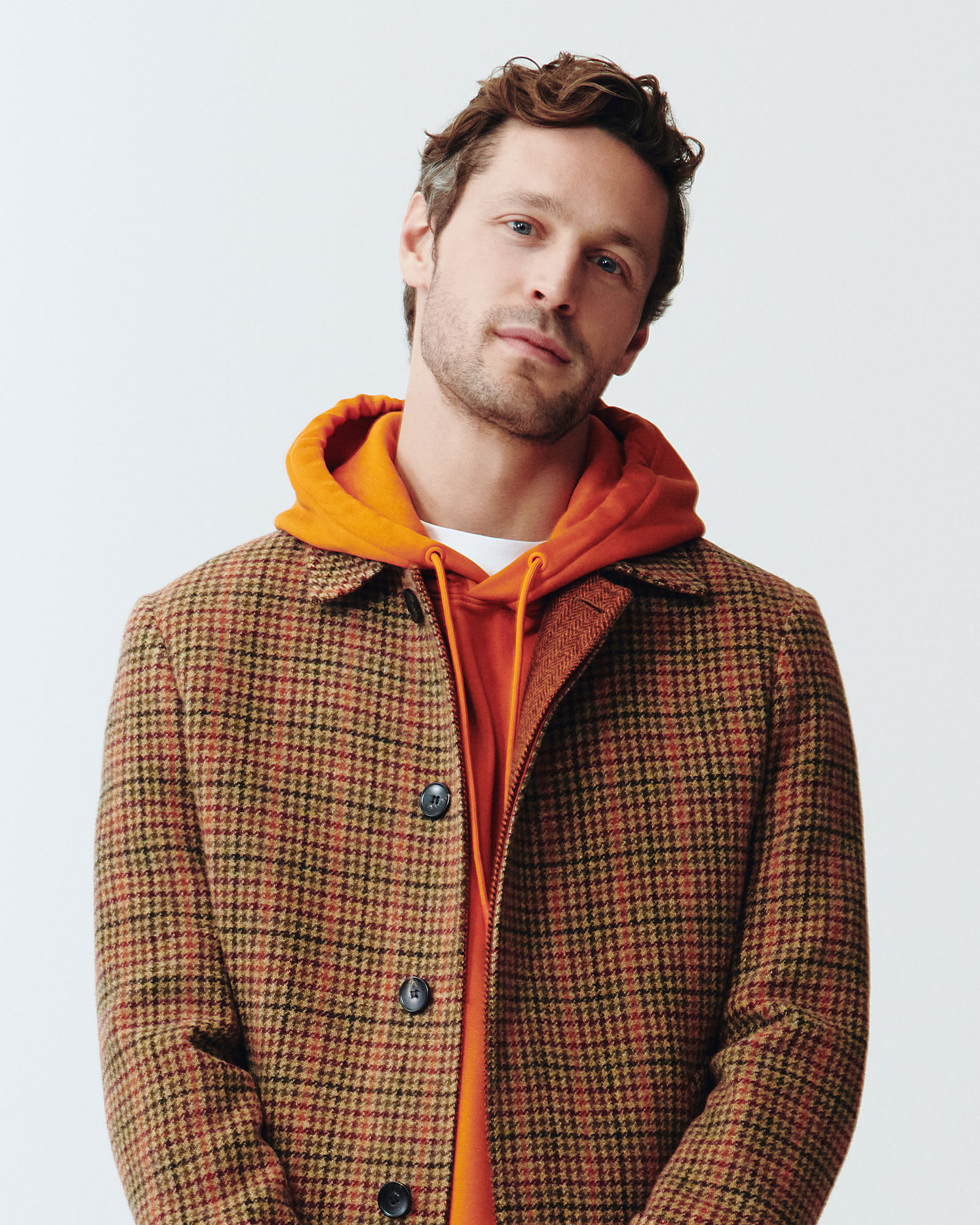 Modello con cappotto a quadri marrone e felpa arancione con cappuccio.