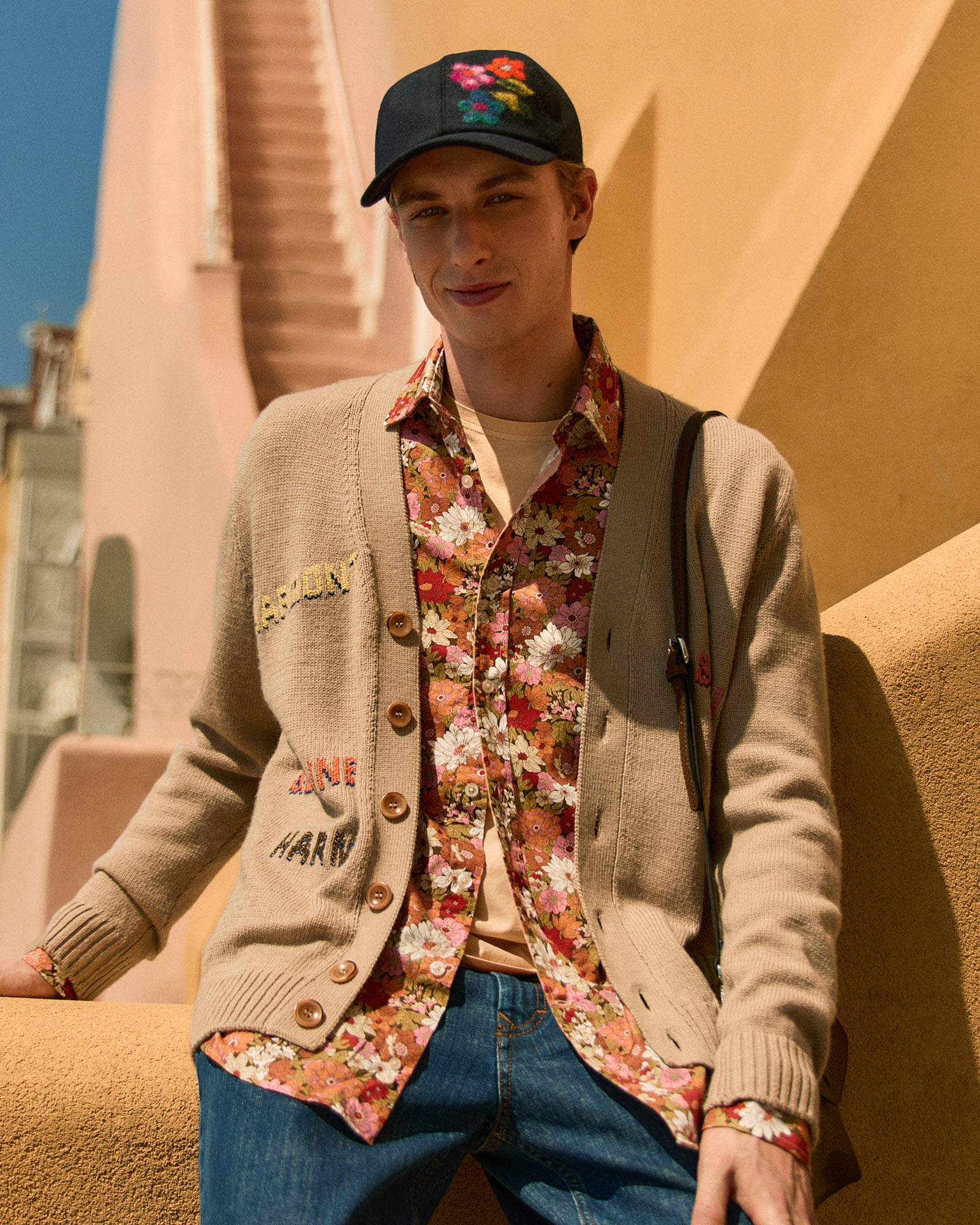 Male model wearing a beige embroidered cardigan and a colorful floral shirt.
