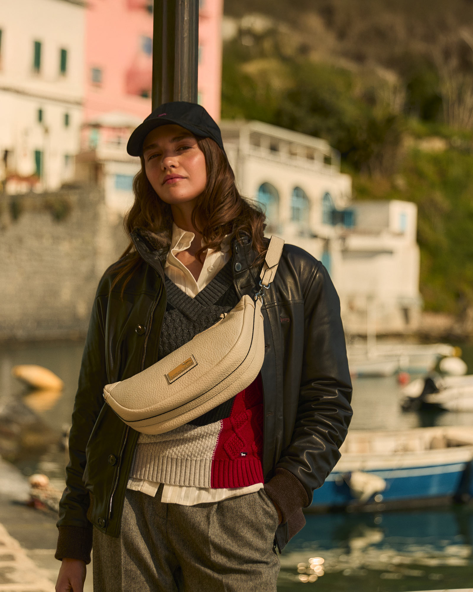 Woman wearing a leather jacket, grey knit vest, and beige shoulder bag.