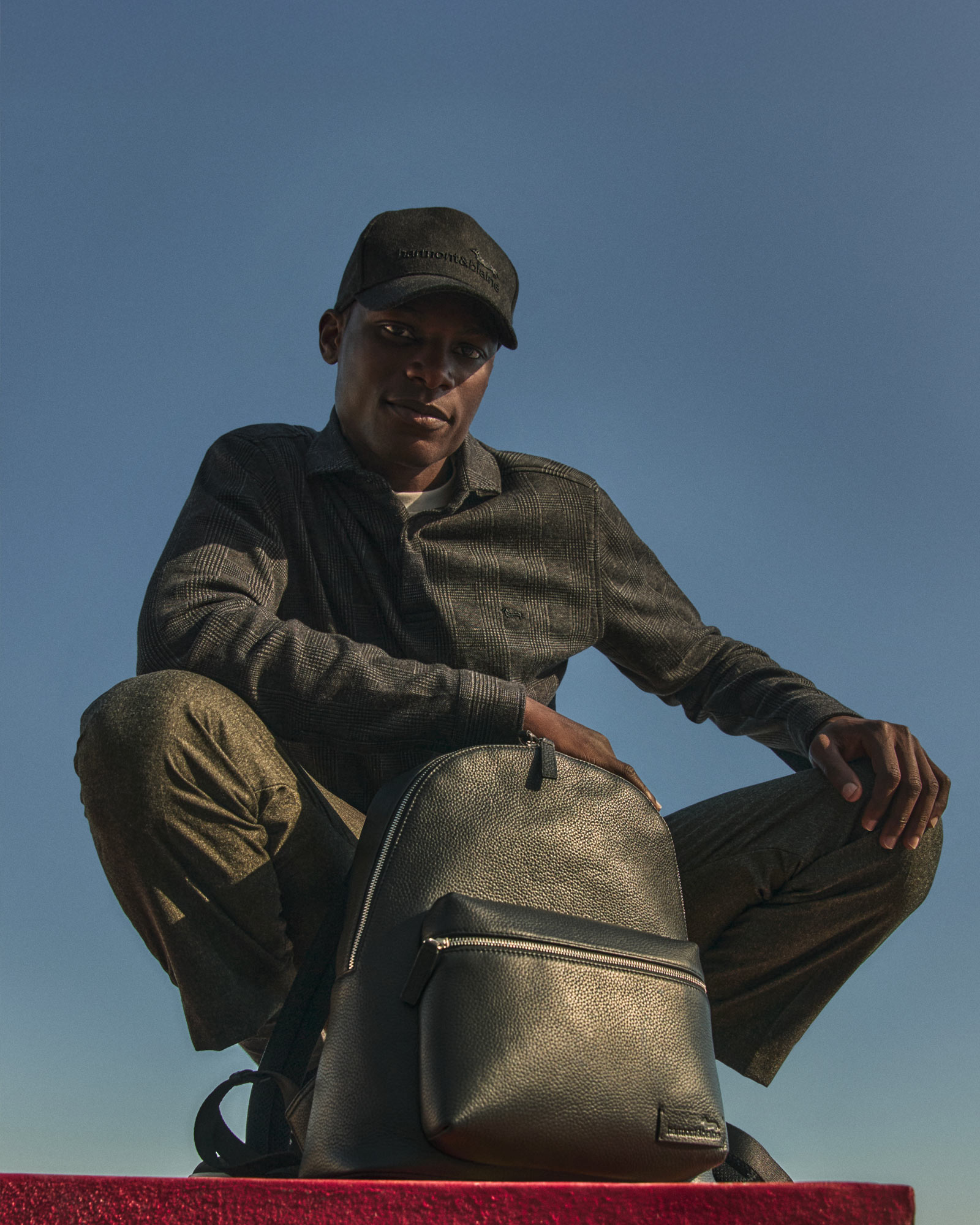 Model wearing a dark shirt with black backpack against blue sky.