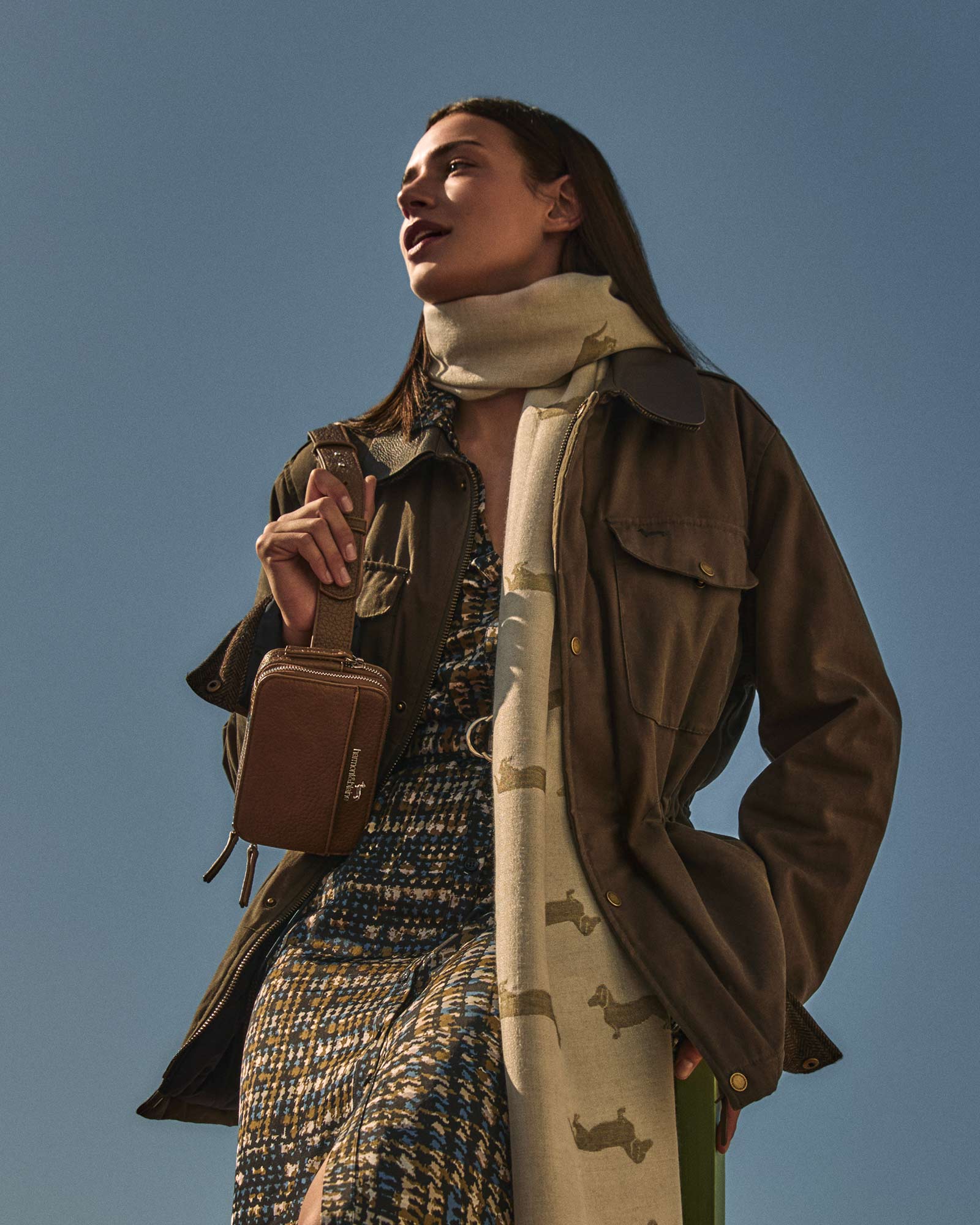 Mujer con chaqueta marrón y bufanda beige con estampado de perro salchicha.