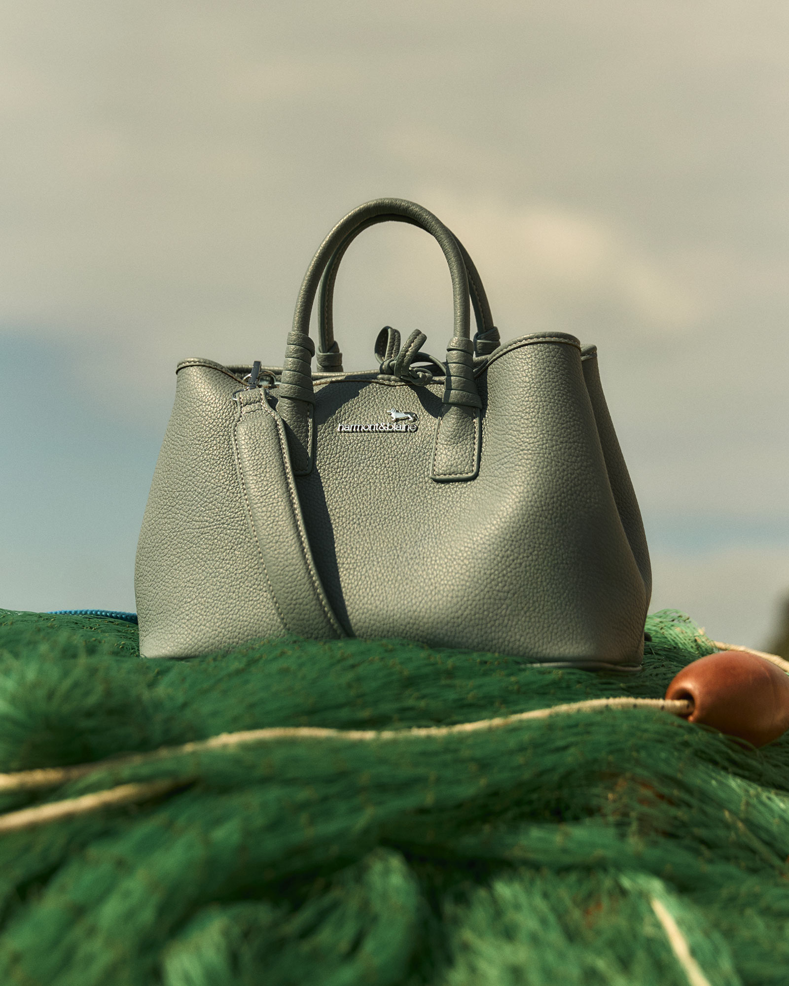 Grey leather handbag placed on green fishing net.