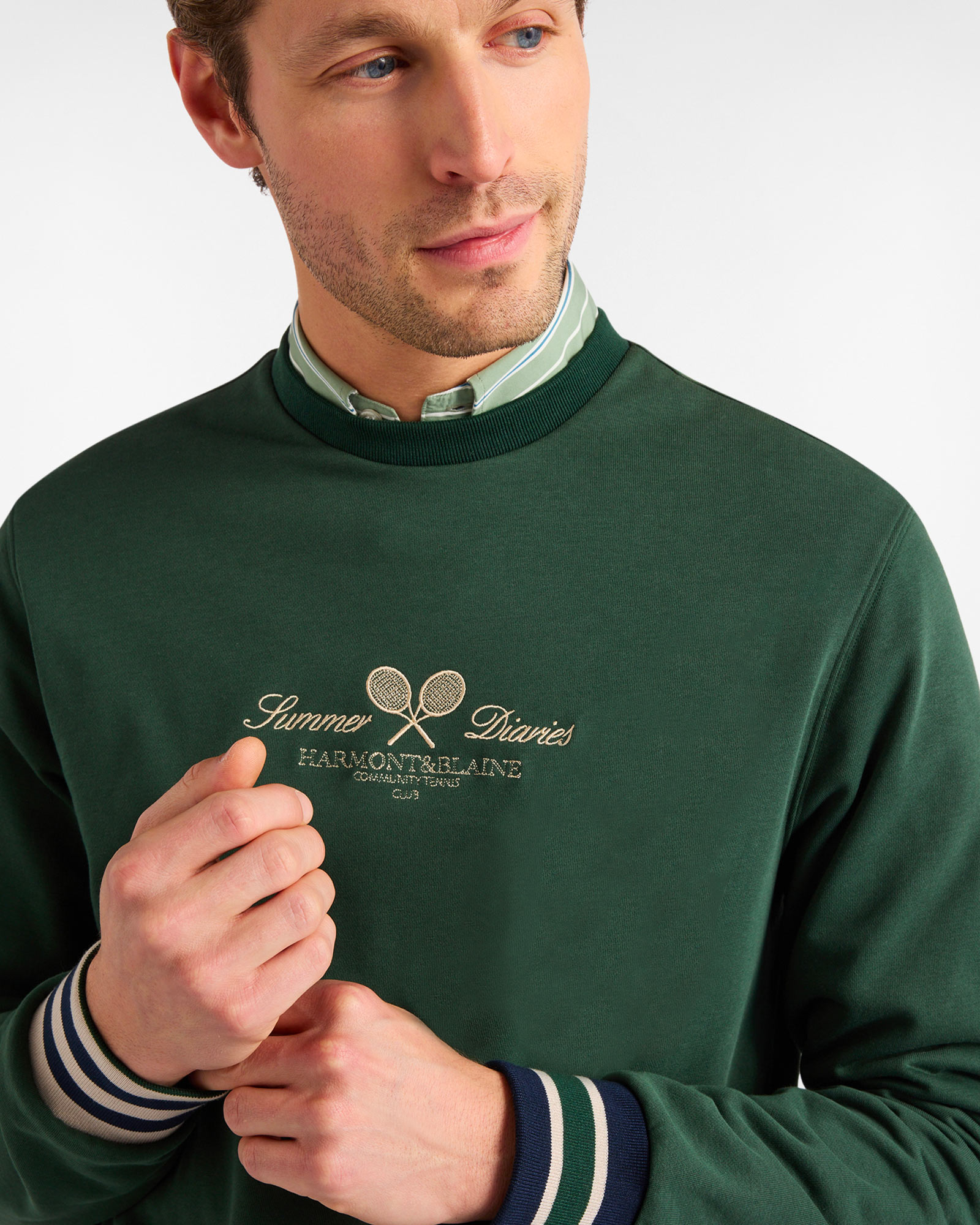 Man wearing a green embroidered sweatshirt over a striped shirt