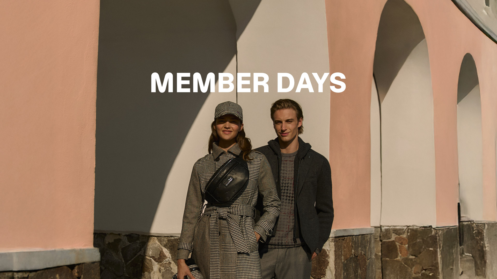 Coppia che iDue persone in posa all’aperto davanti a un edificio con archi, indossano capi invernali Harmont & Blaine. Testo ‘MEMBER DAYS’ in alto, immagine che promuove l’anticipo dei saldi riservato ai clienti registrati.ndossa cappotti invernali davanti a un grande fiore blu.