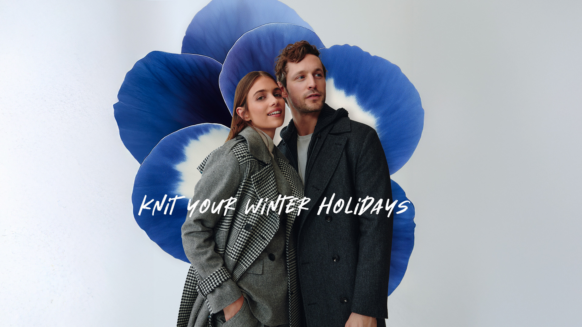 Pareja con abrigos de invierno frente a una gran flor azul.