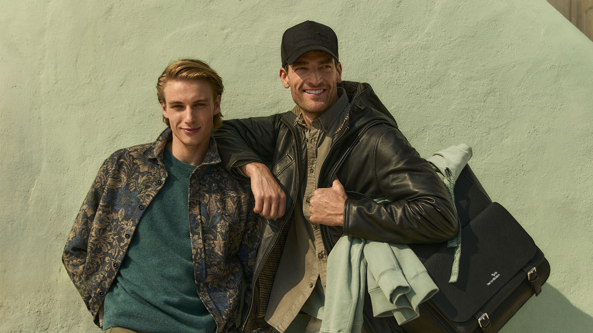 Two men in fall outfits in front of a green wall
