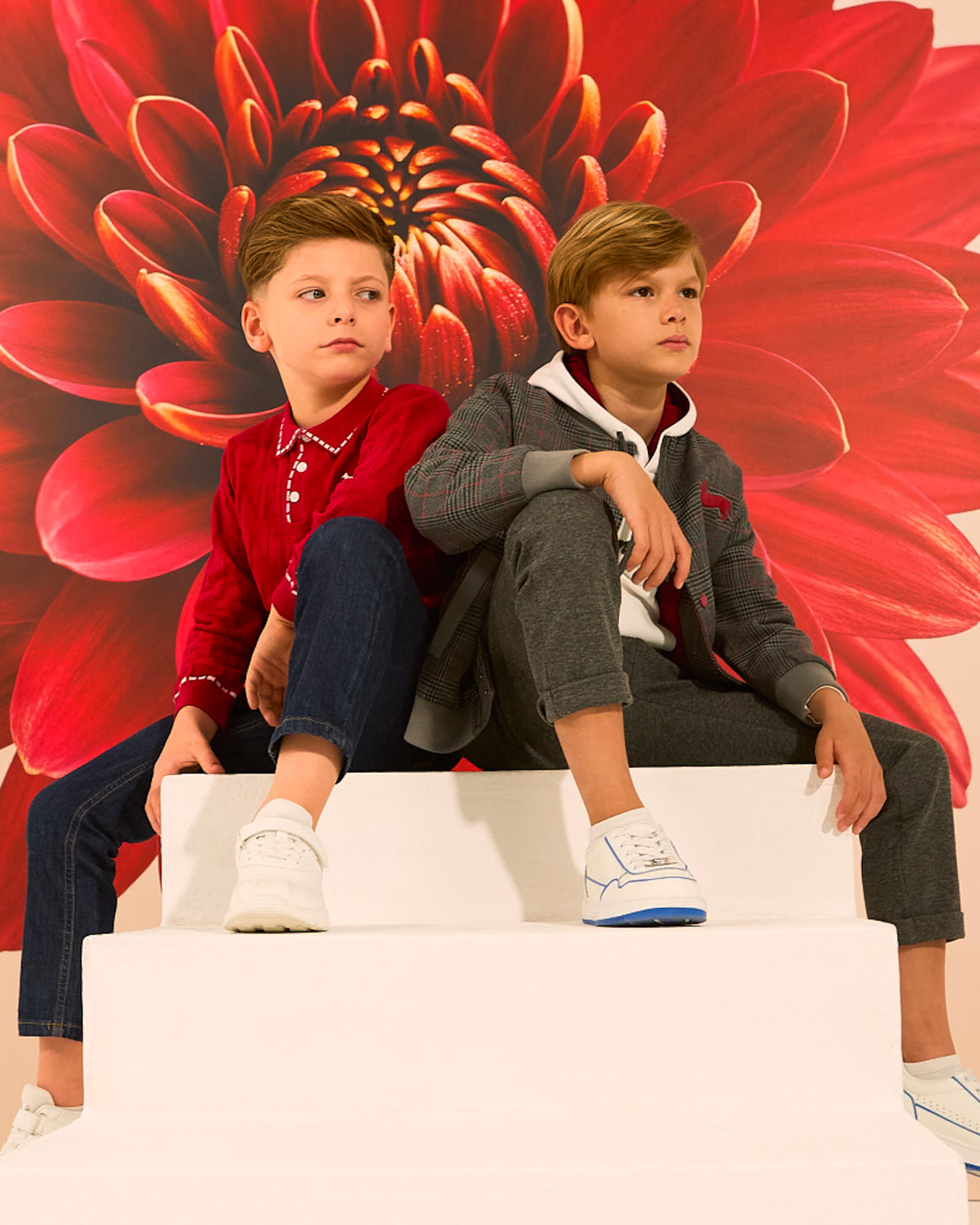 Due bambini seduti con abbigliamento casual, sfondo chiaro.