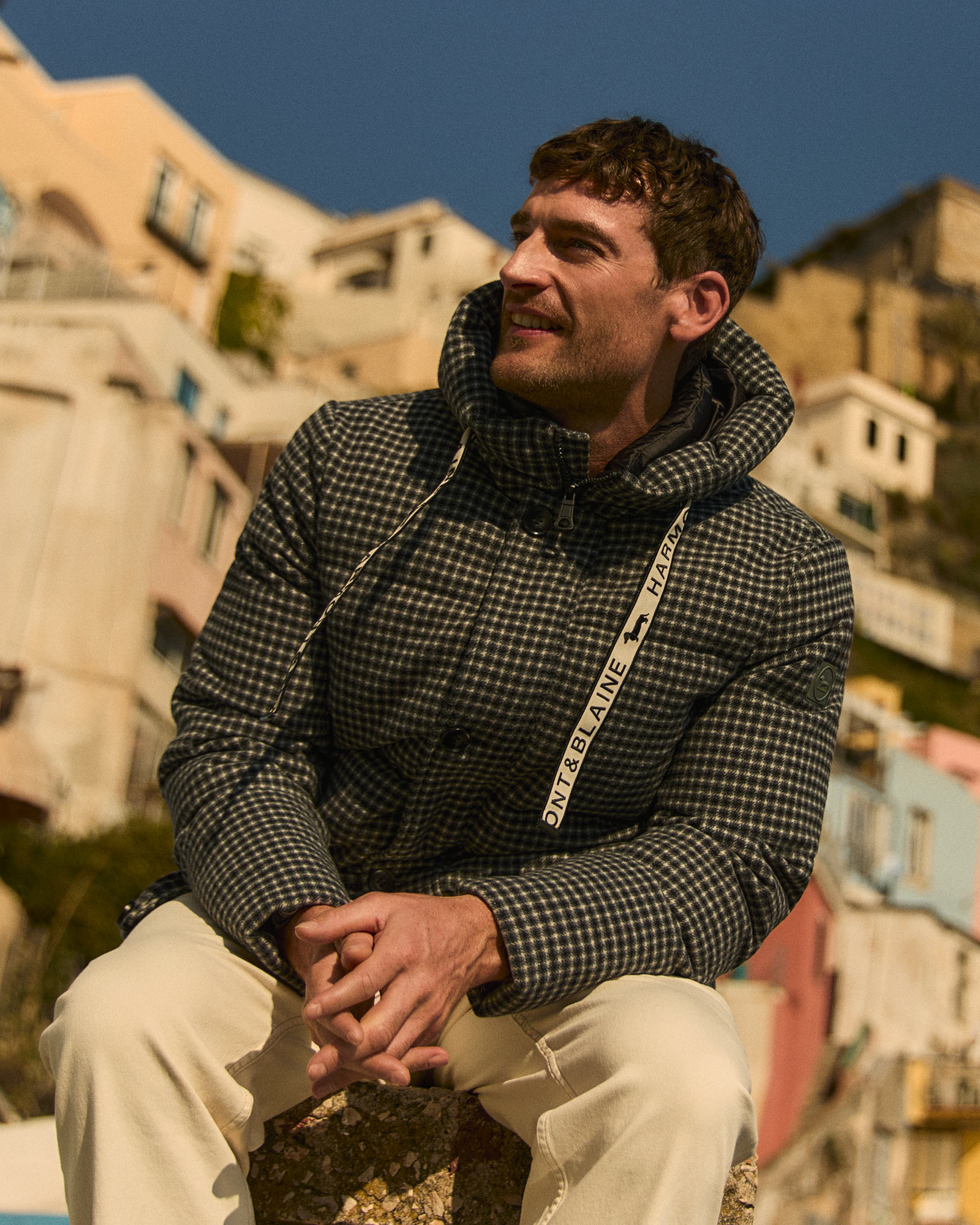 Uomo indossa giacca imbottita a quadri con pantaloni chiari.