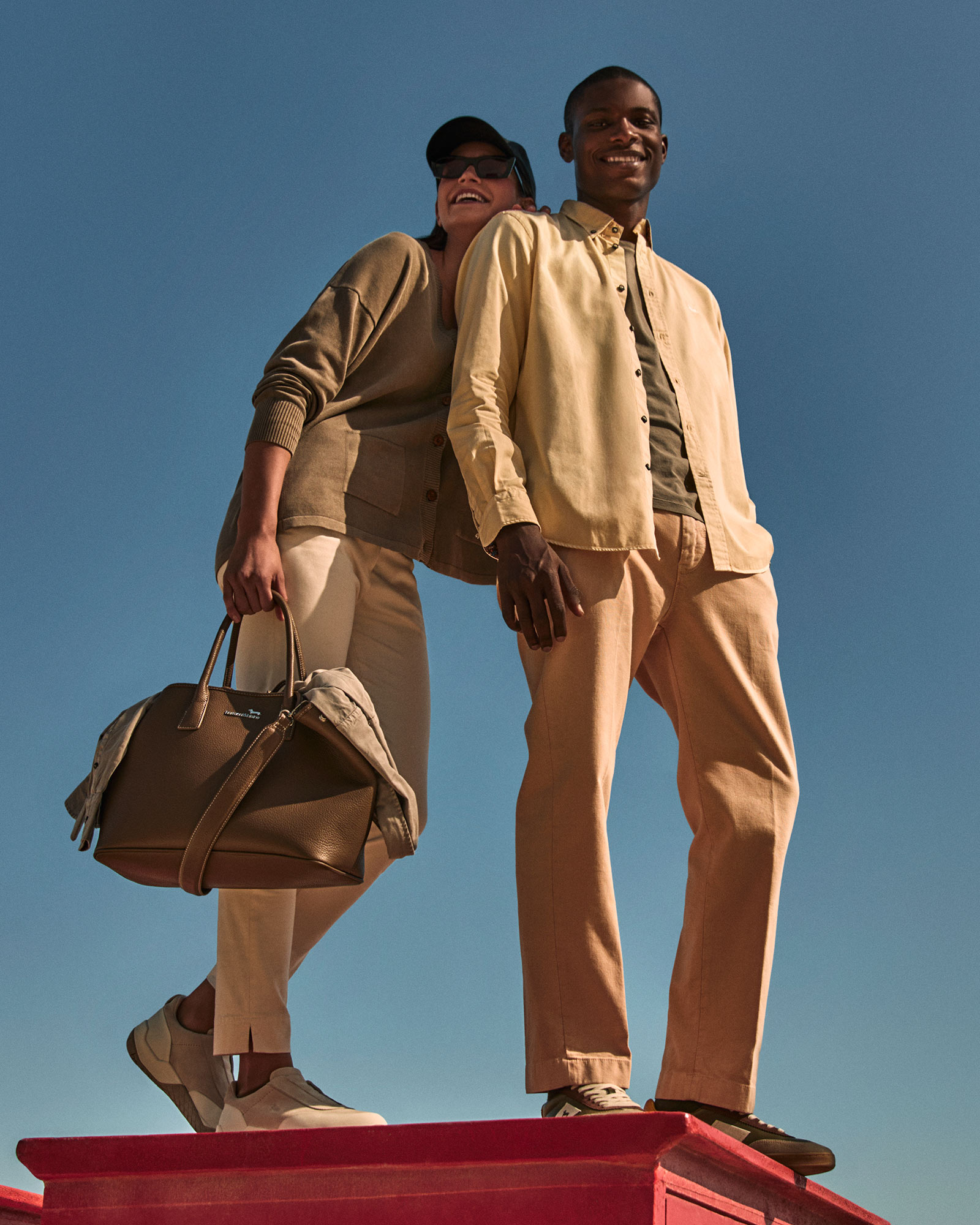 Modello uomo e donna sorridenti con look casual nei toni del beige e giallo chiaro.