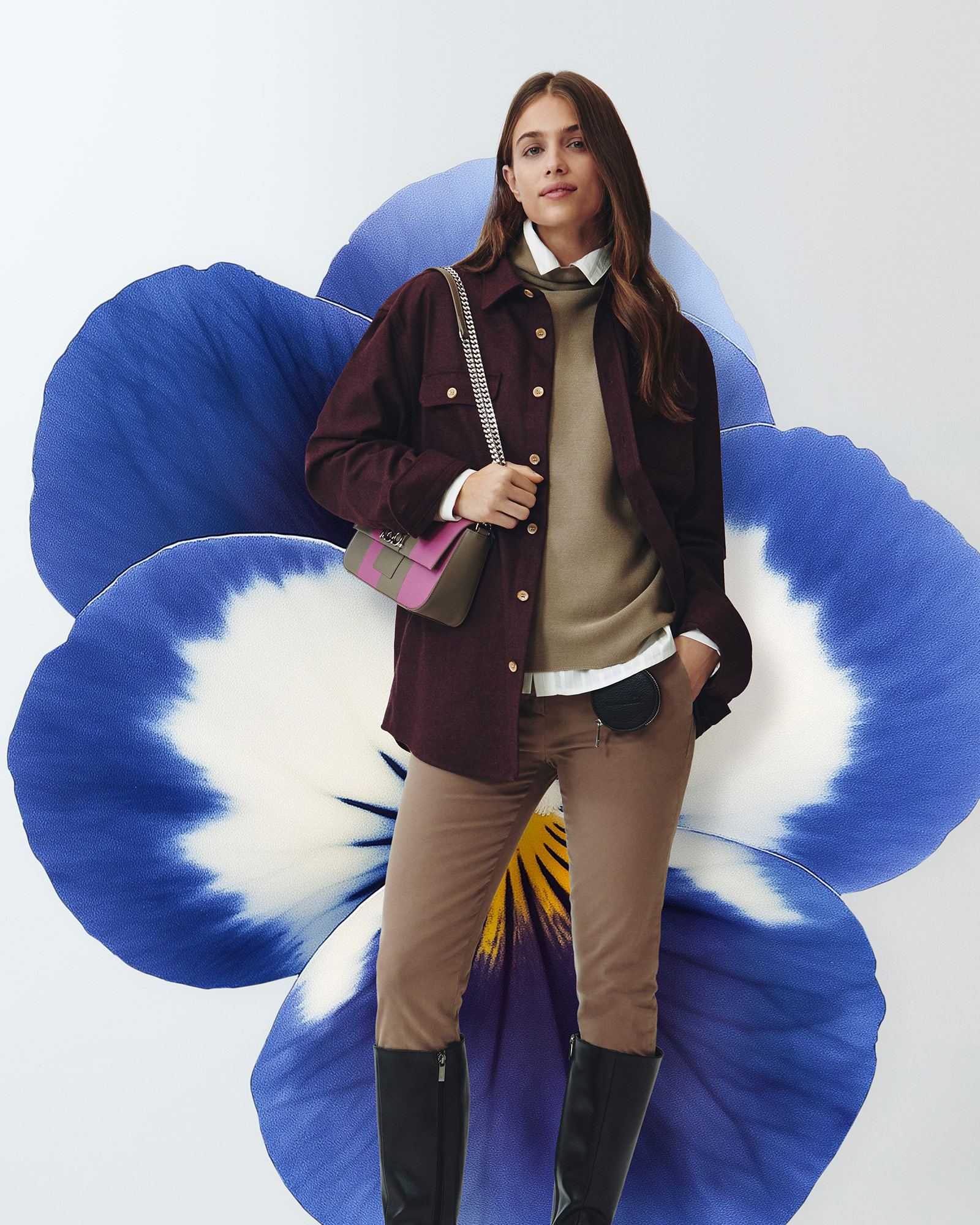 Mujer con camisa beige y chaqueta burdeos frente a una gran flor azul.